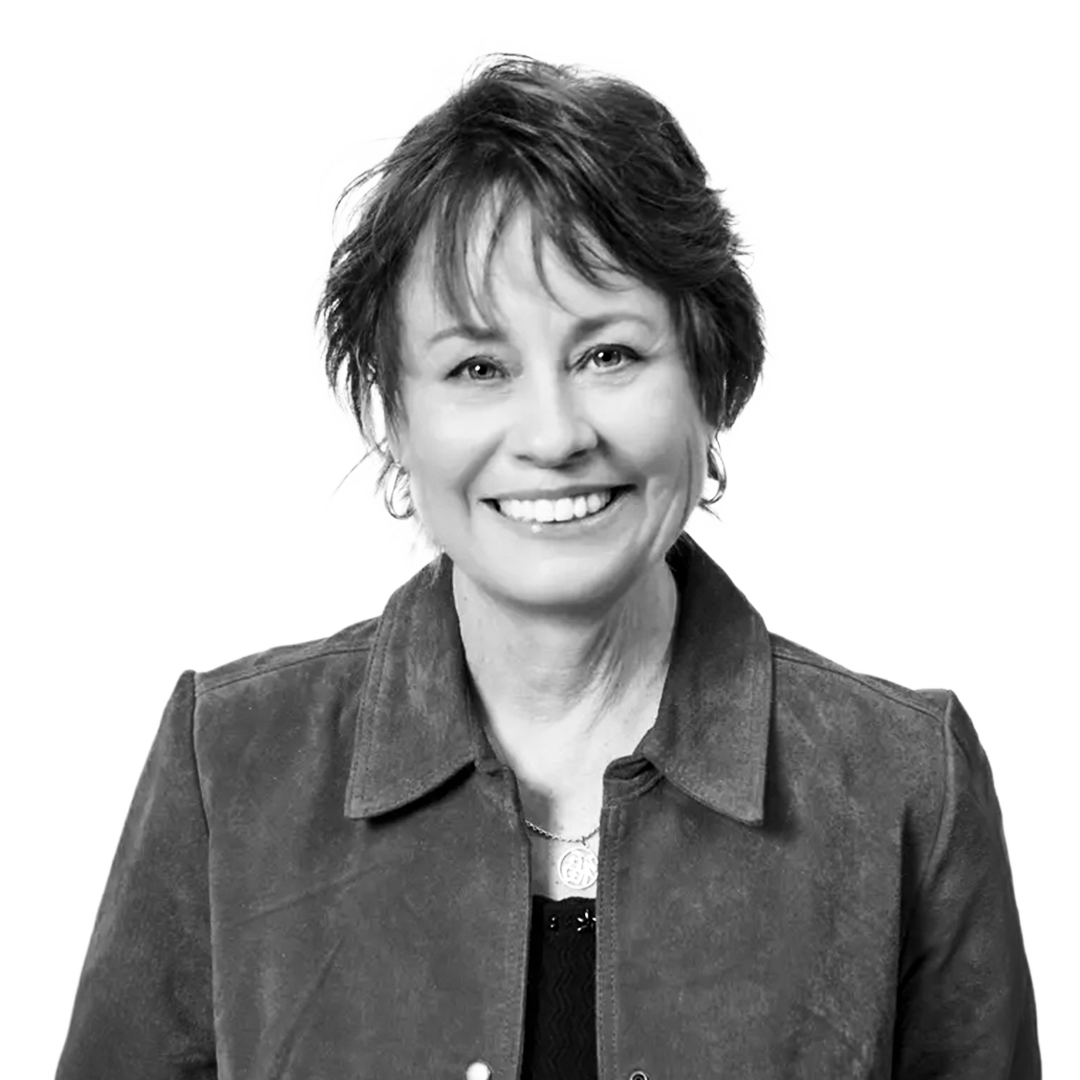 Black and white portrait of a smiling woman with short, tousled hair, wearing a collared shirt and jacket.
