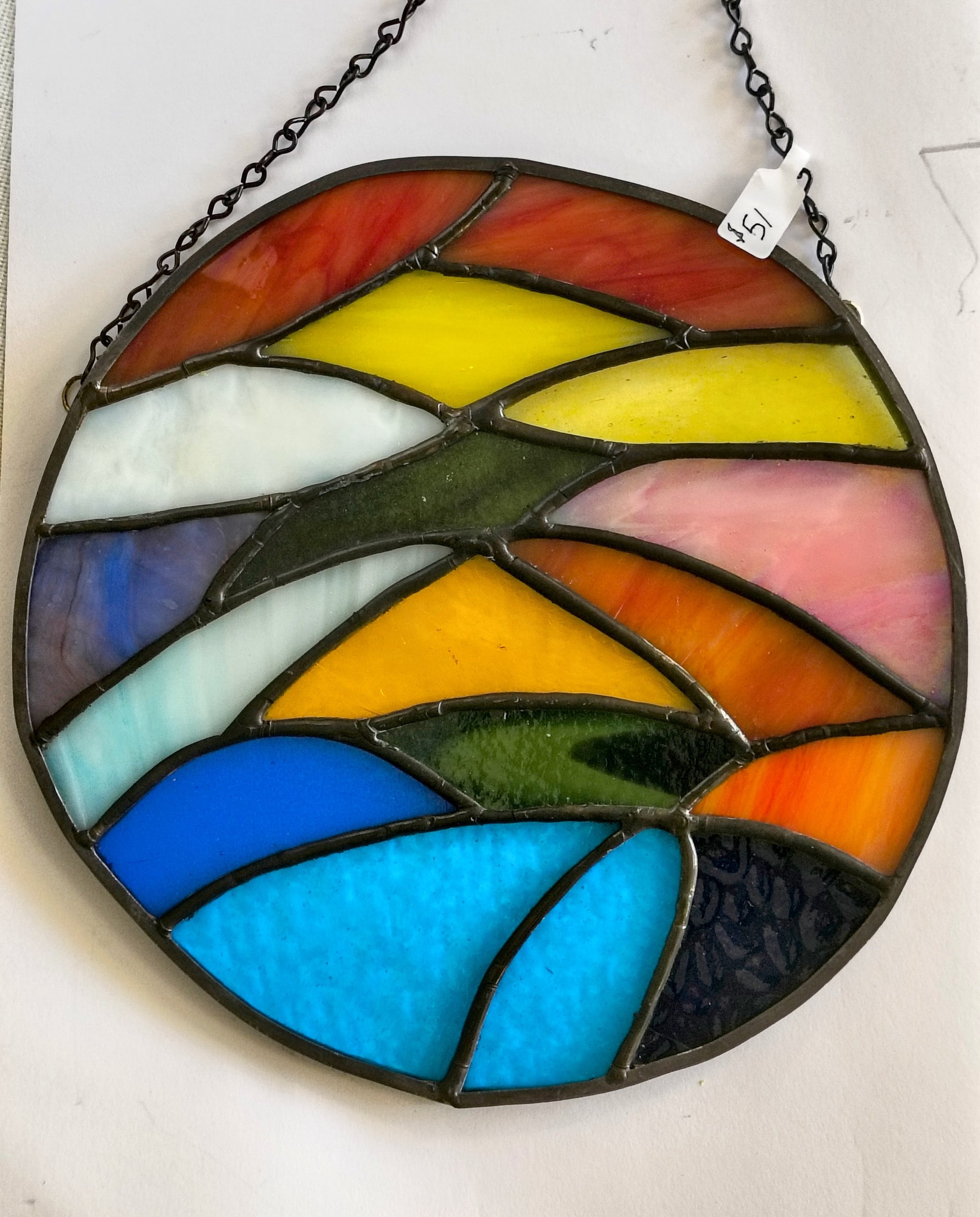 Decorative butterfly-shaped necklace with orange and black stained glass wings, outlined with a metal frame and small white dots, on a black string.
