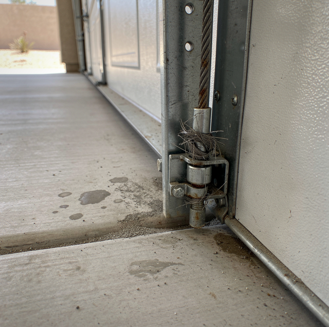 Close-up of a sliding glass door frame and latch mechanism on a concrete floor with debris visible.