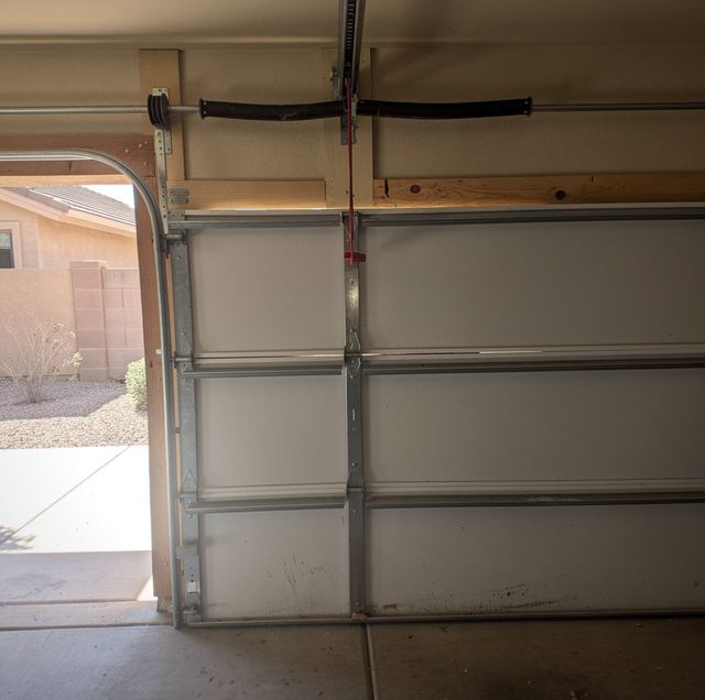 Bent garage door hinge separating two misaligned white steel sections