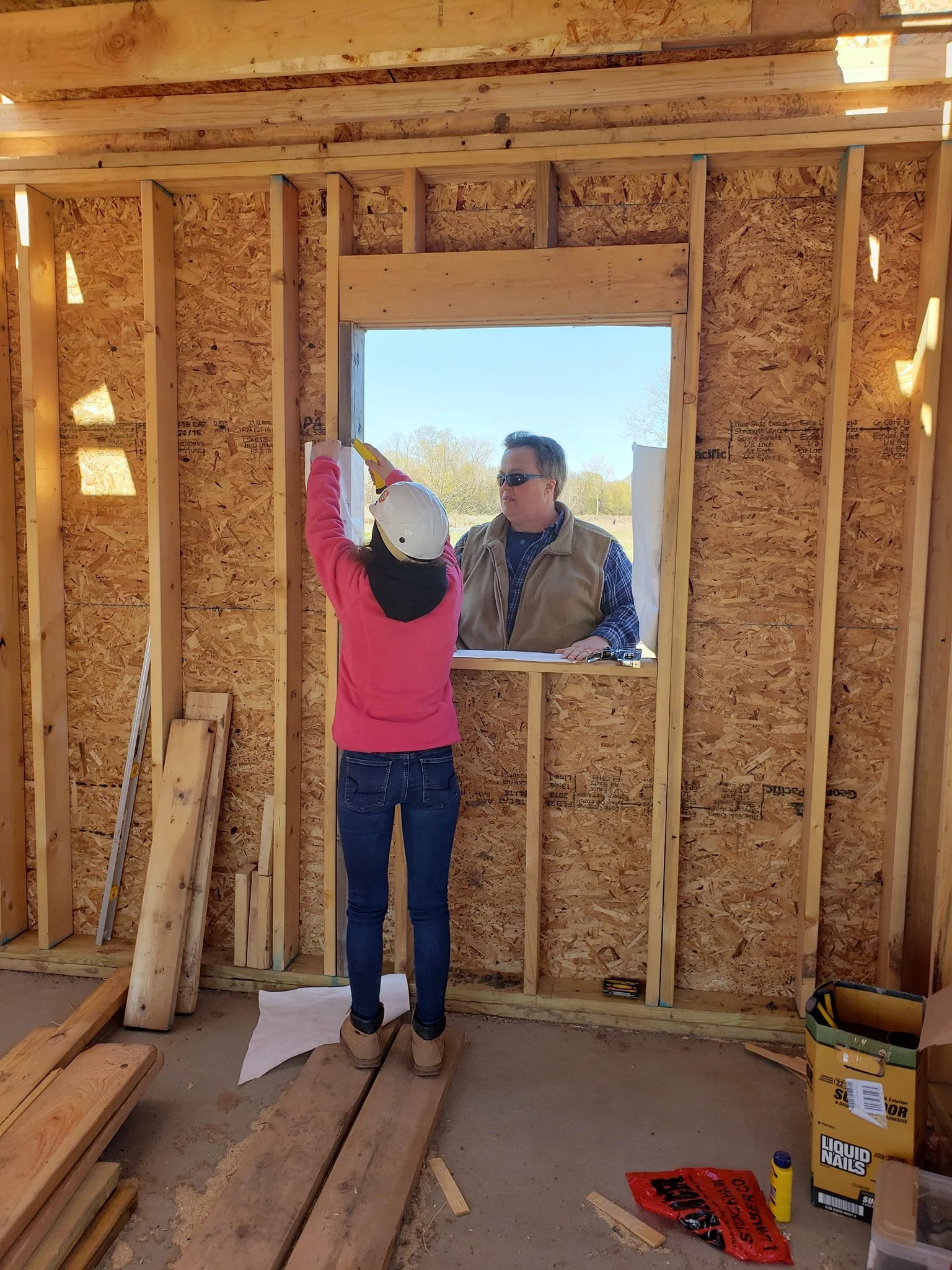 Student from Holley Schools working in a construction site with teacher on other side of unfinished window. 