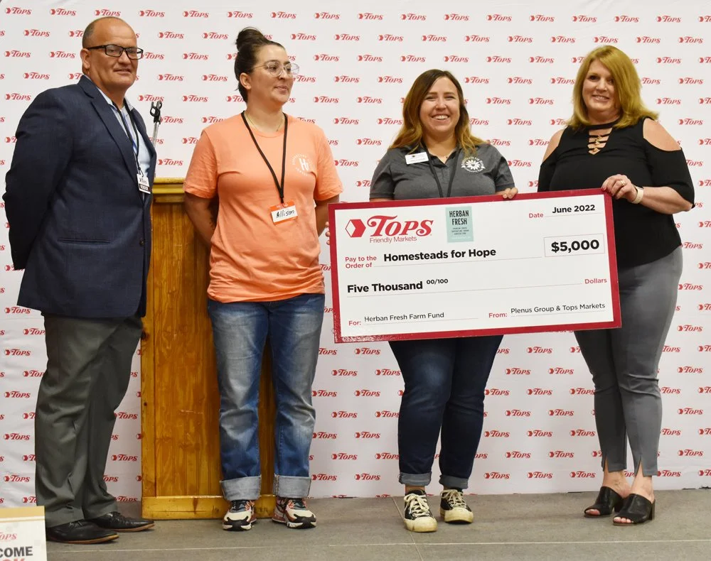 Four people holding a large check donation from Tops Supermarket.