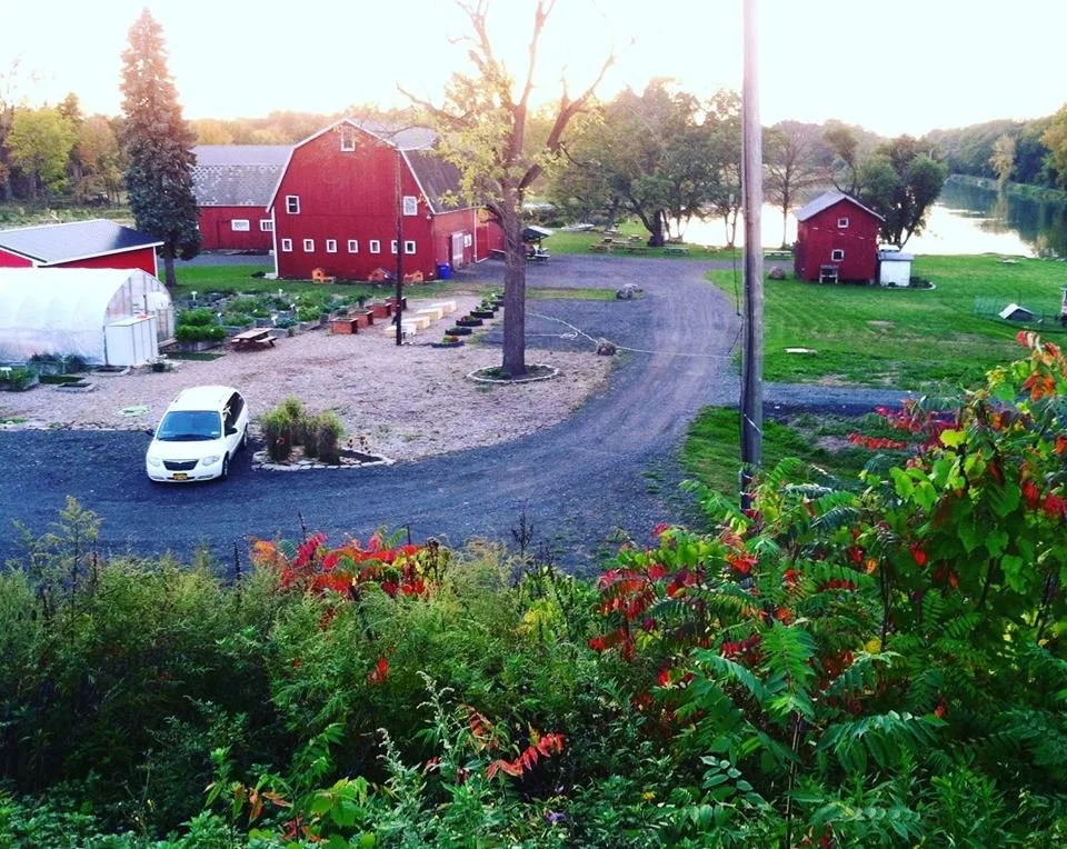 Homesteads for Hope Farm with Green House and Barn and setting sun and Erie Canal in the background. 