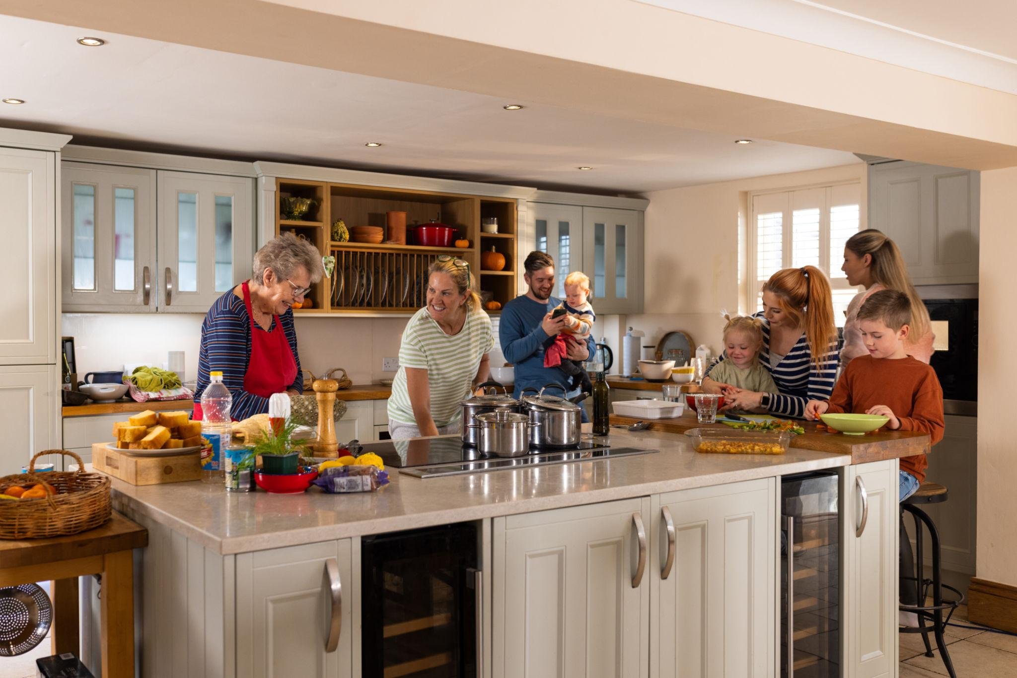 Three generations of a family gathered in a spacious modern kitchen preparing a meal together around a large island.