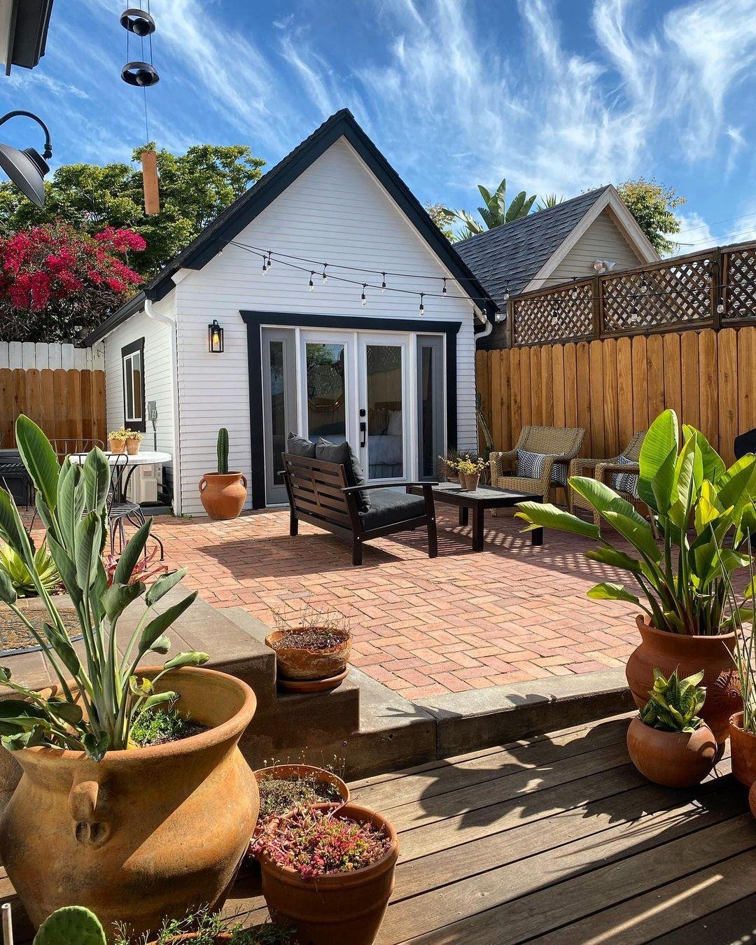 A small white accessory dwelling unit (ADU) with a brick patio, outdoor seating, and string lights in a private backyard.