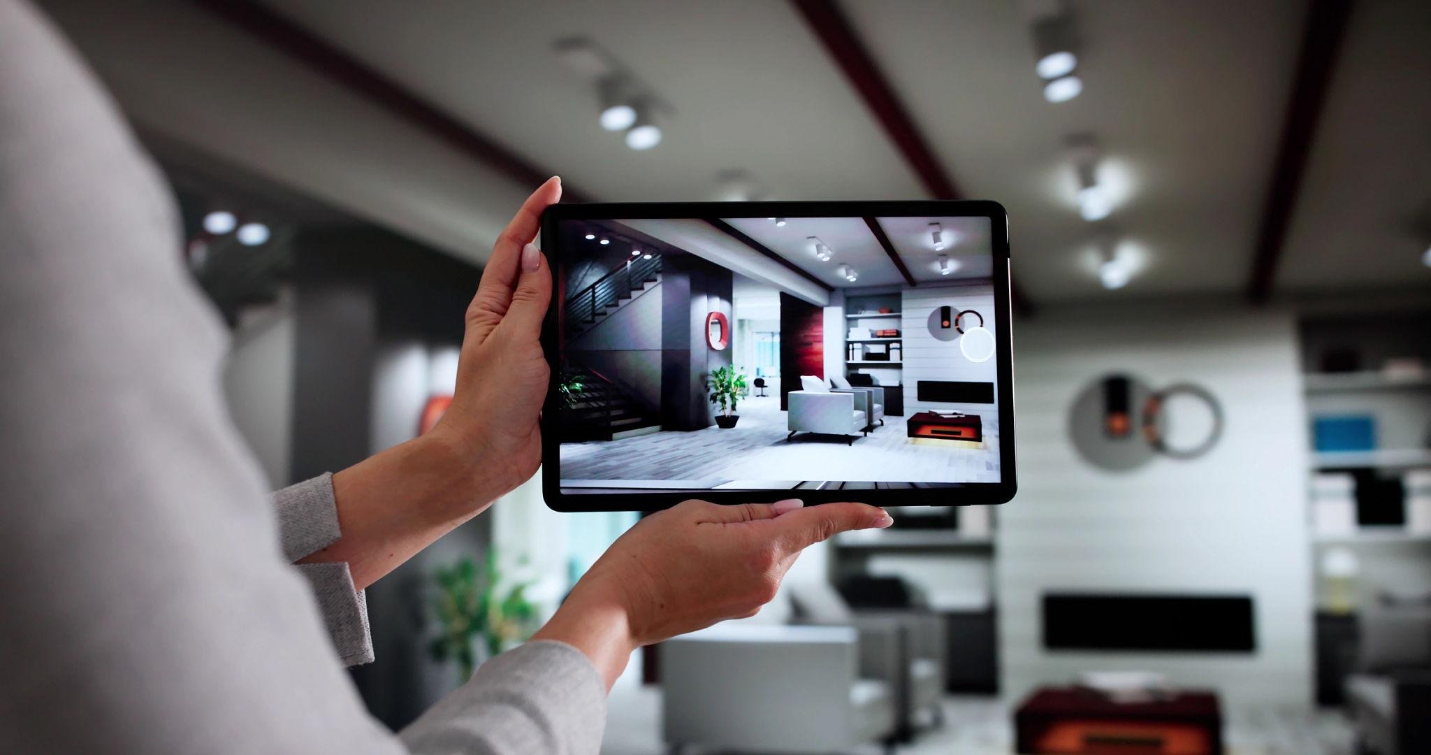 person holding a tablet displaying an augmented reality 3D interior design model of a modern living room.