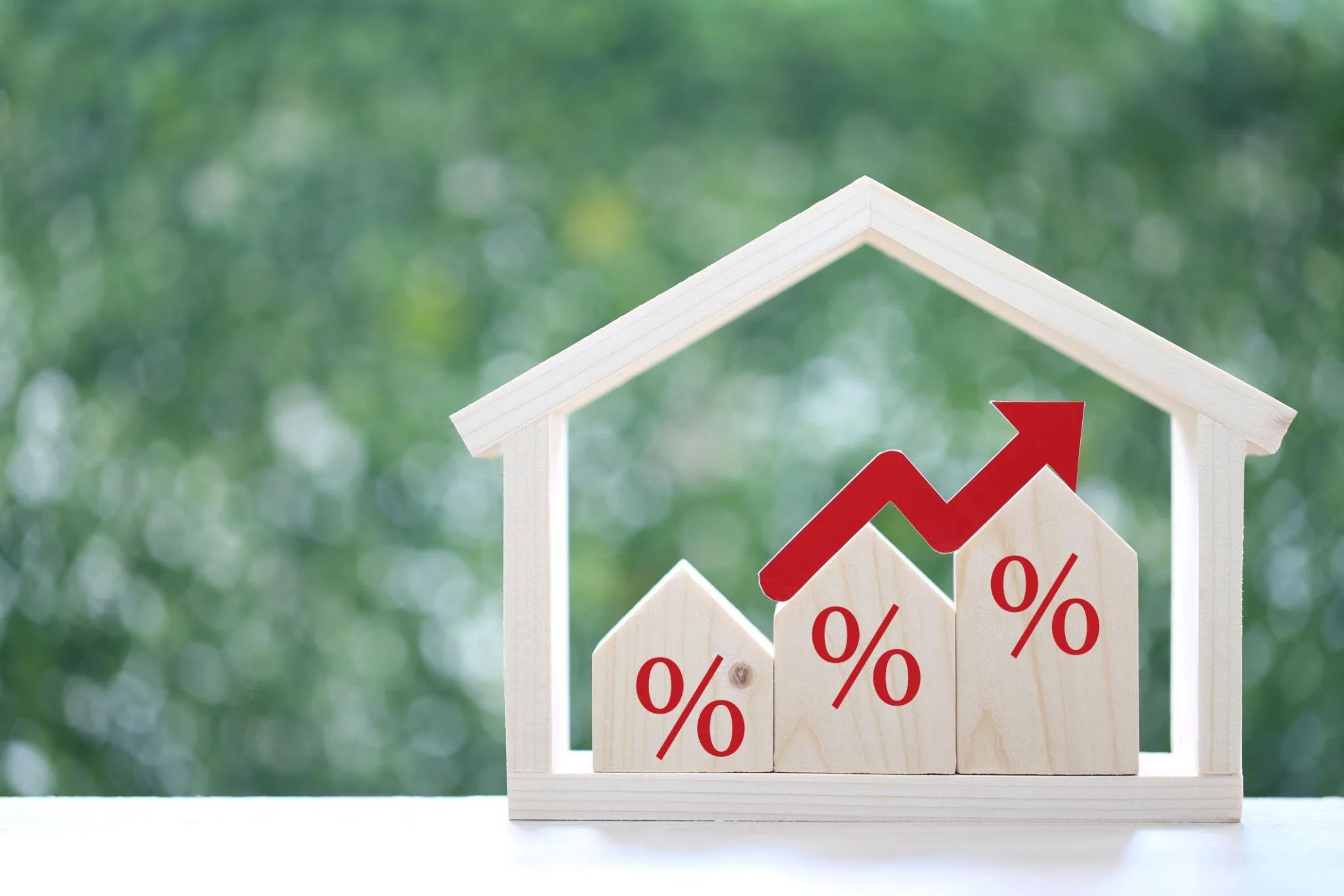 Wooden house models with percentage symbols and an upward arrow representing rising mortgage interest rates and housing market trends