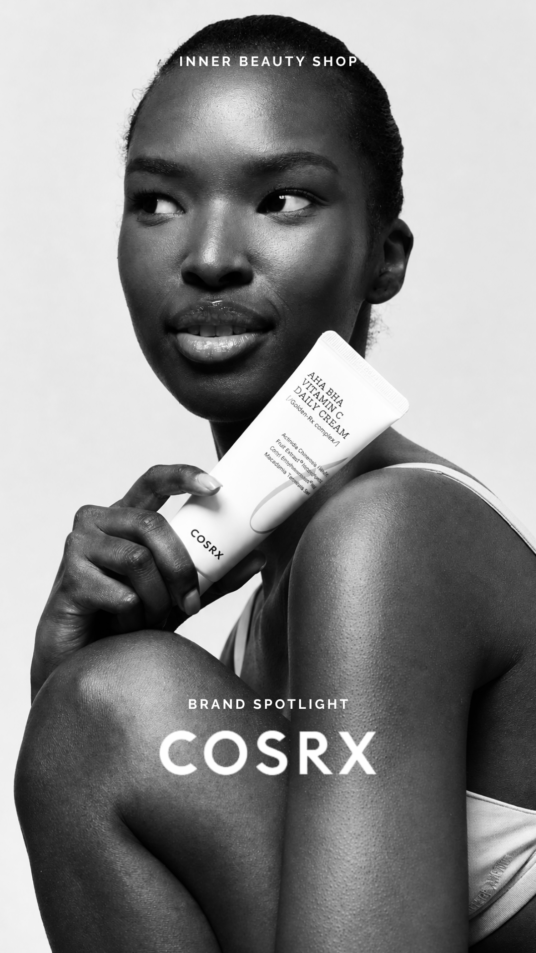 Black and white image of a woman with smooth skin holding a COSRX vitamin C daily cream tube near her face. She has a confident expression and is looking off to the side. The text 