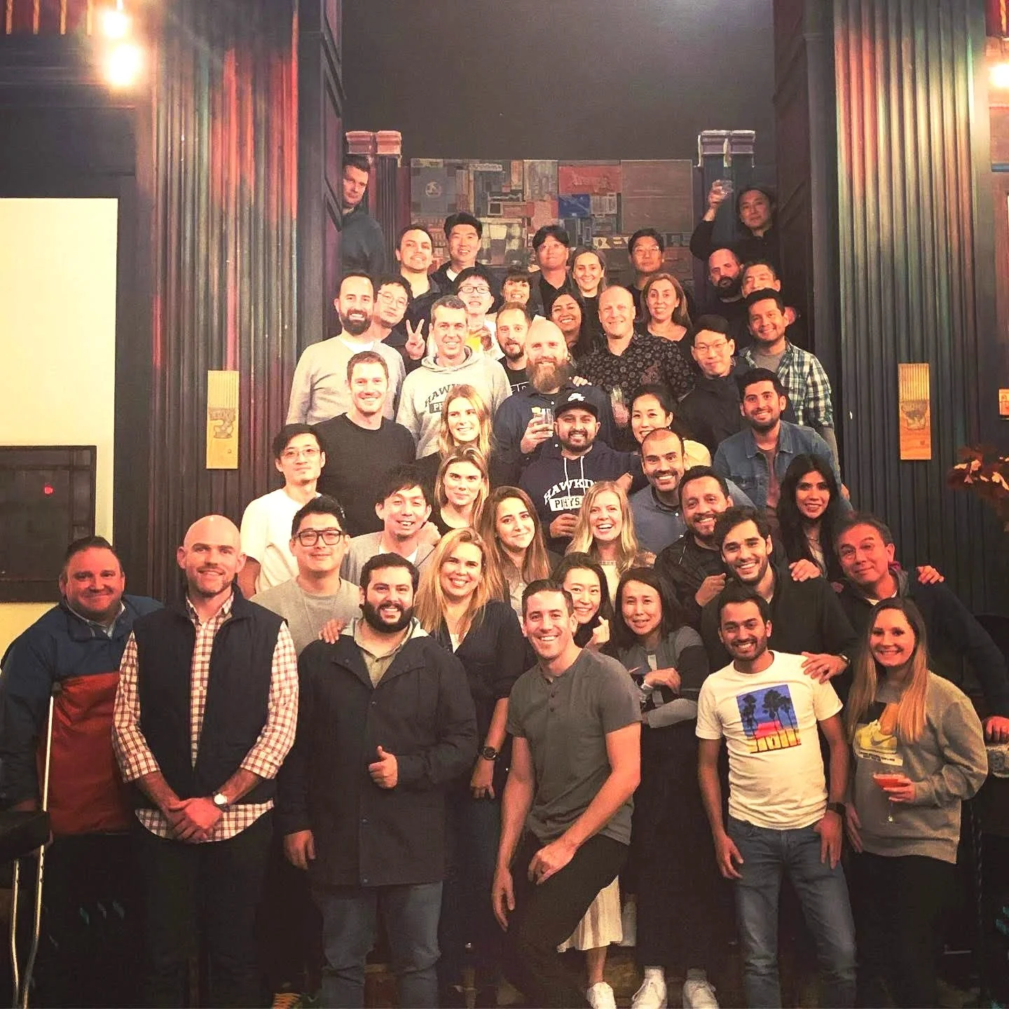 A large group of people gathered together on a staircase inside a dimly lit venue, smiling and posing for a group photo.