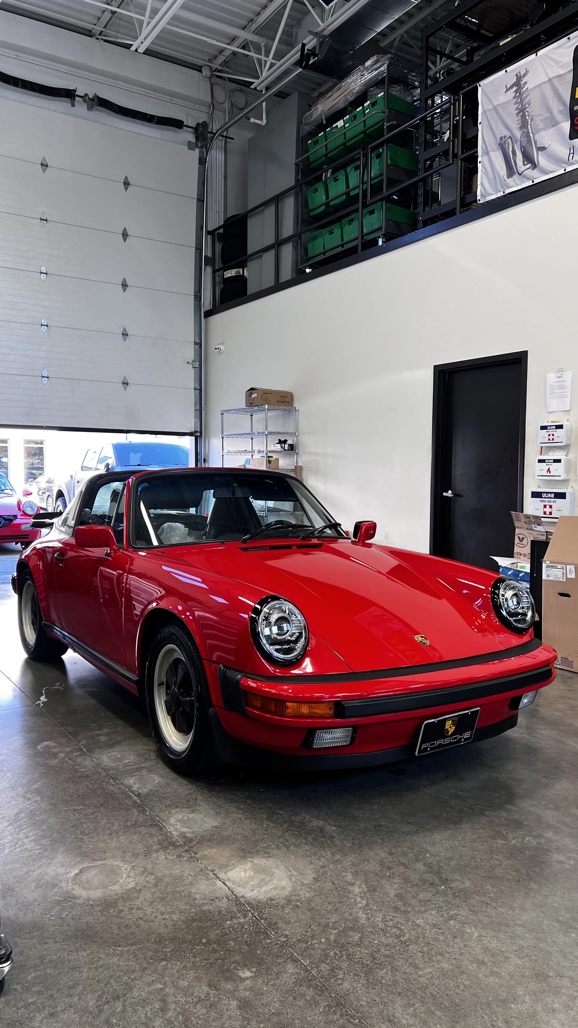 A red vintage Porsche 911 convertible parked inside a garage or showroom.
