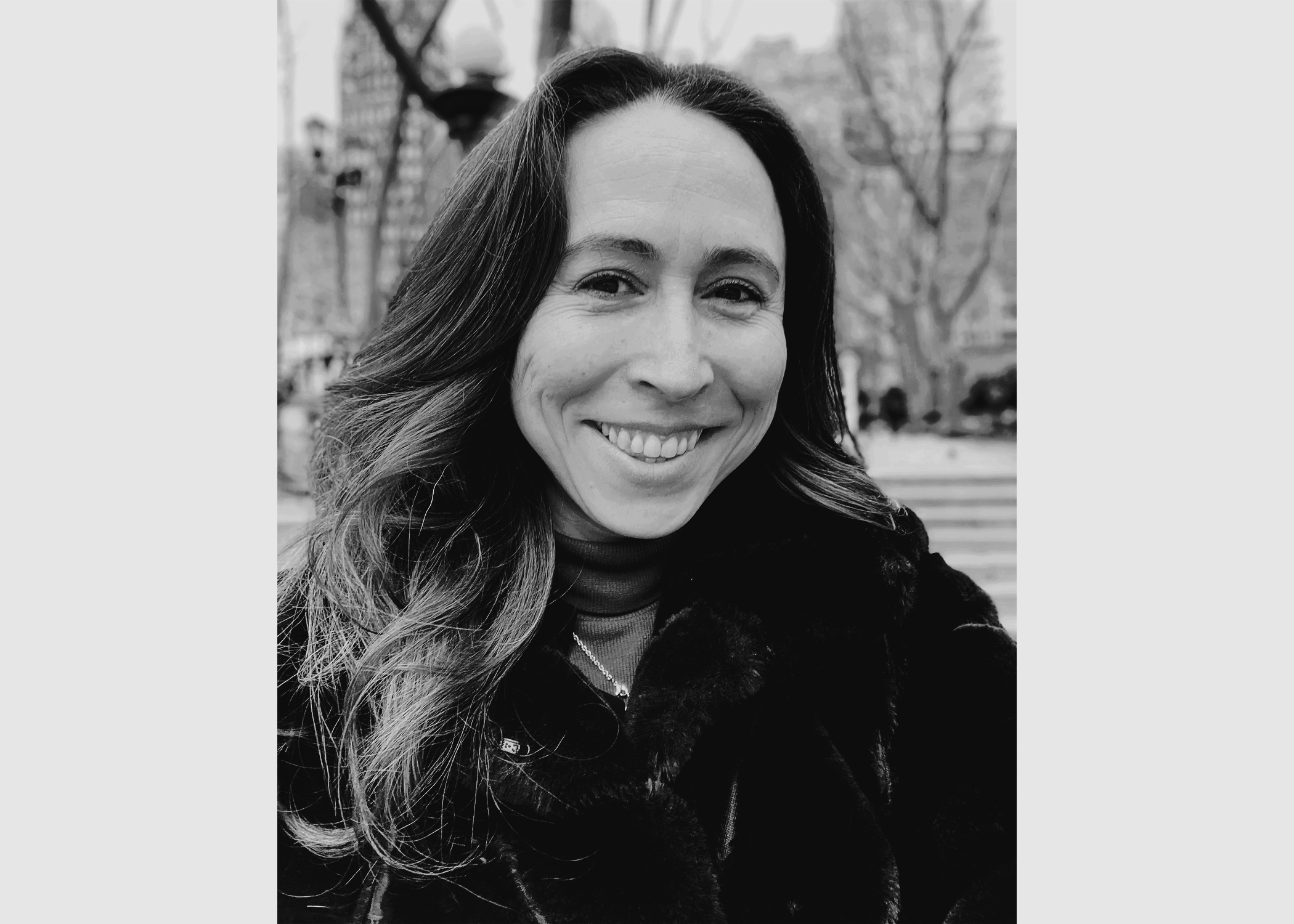 A young woman with her hair down, smiling with a view of the city behind her.