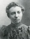 Black and white portrait of a woman with curly hair, wearing a high-collared blouse and a string of beads.