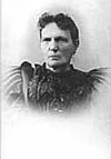 Black and white photo of a woman with dark hair, wearing a dark dress with puffed sleeves.