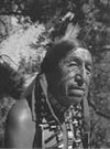 Black and white photo of a Native American woman outdoors with trees in the background.