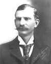 Black and white portrait of a man with neatly combed hair, wearing a suit and tie.