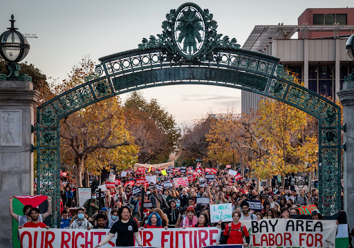 Thousands of workers march through the main gates of UC Berkeley. At the front of the march, workers hold a banner that reads: "Our Rights Our Future" in red letters.