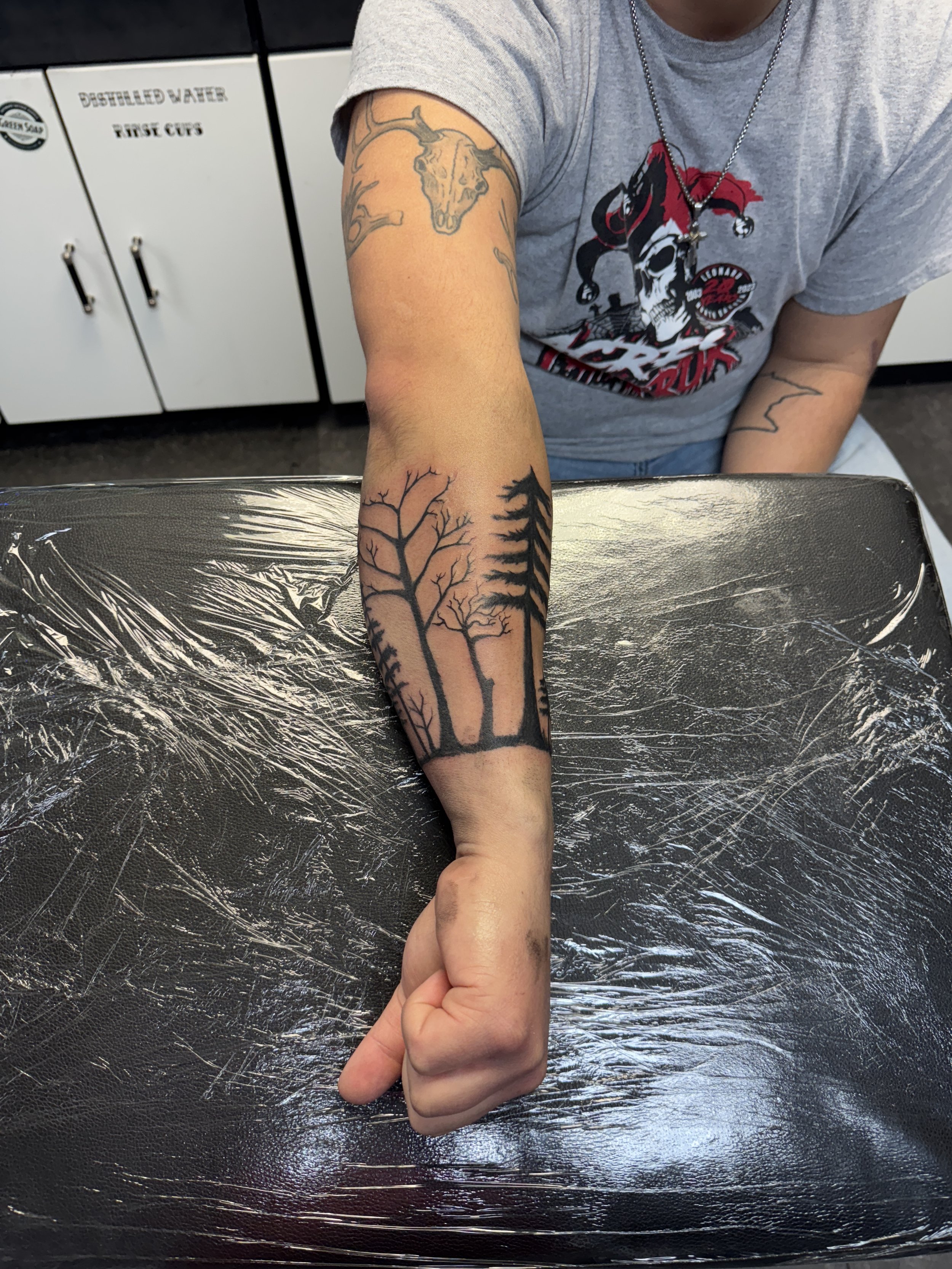 Tattoo of leafless trees on person's forearm at tattoo parlor.