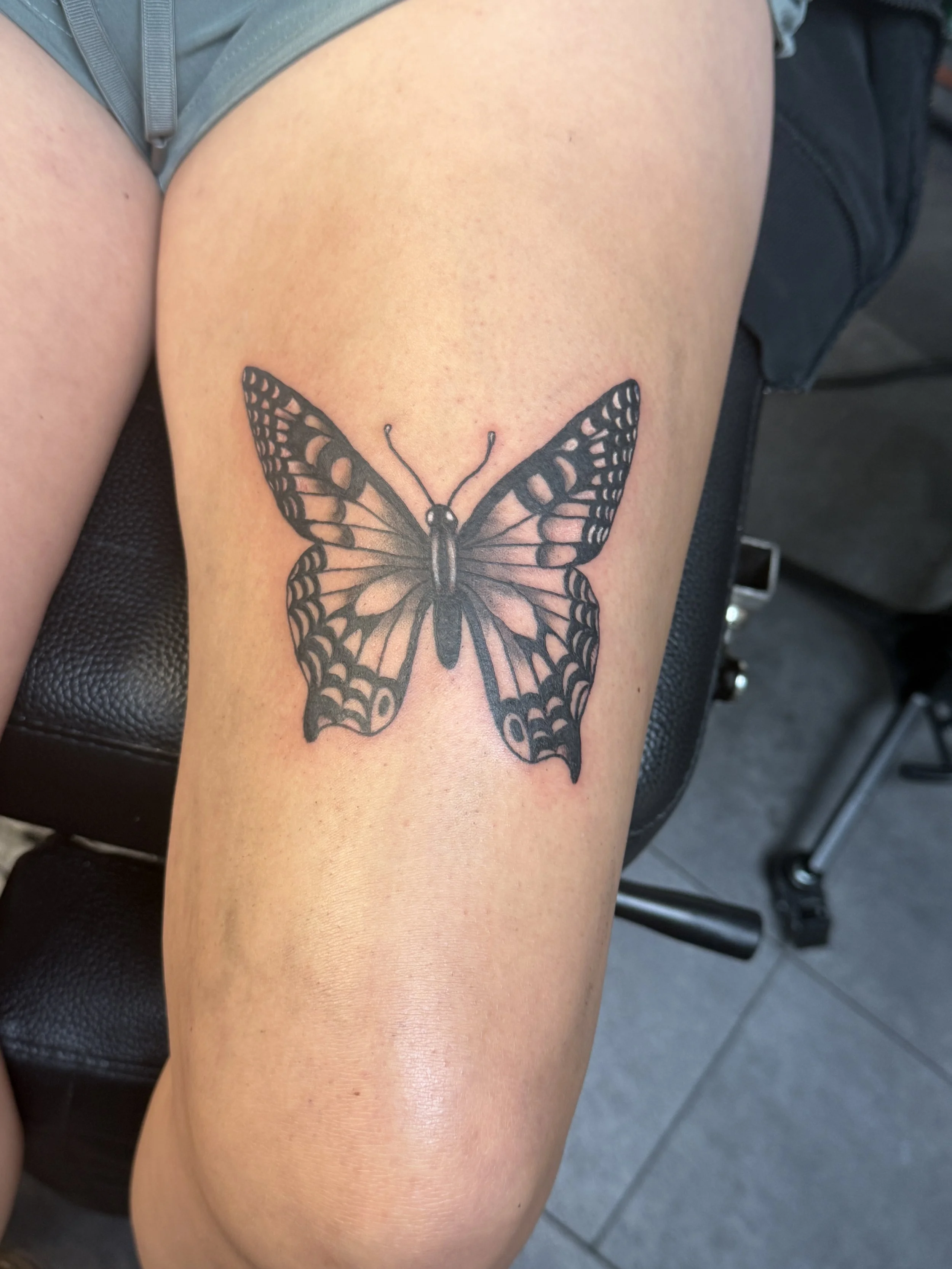 A butterfly tattoo with black and white shading on a person's thigh.