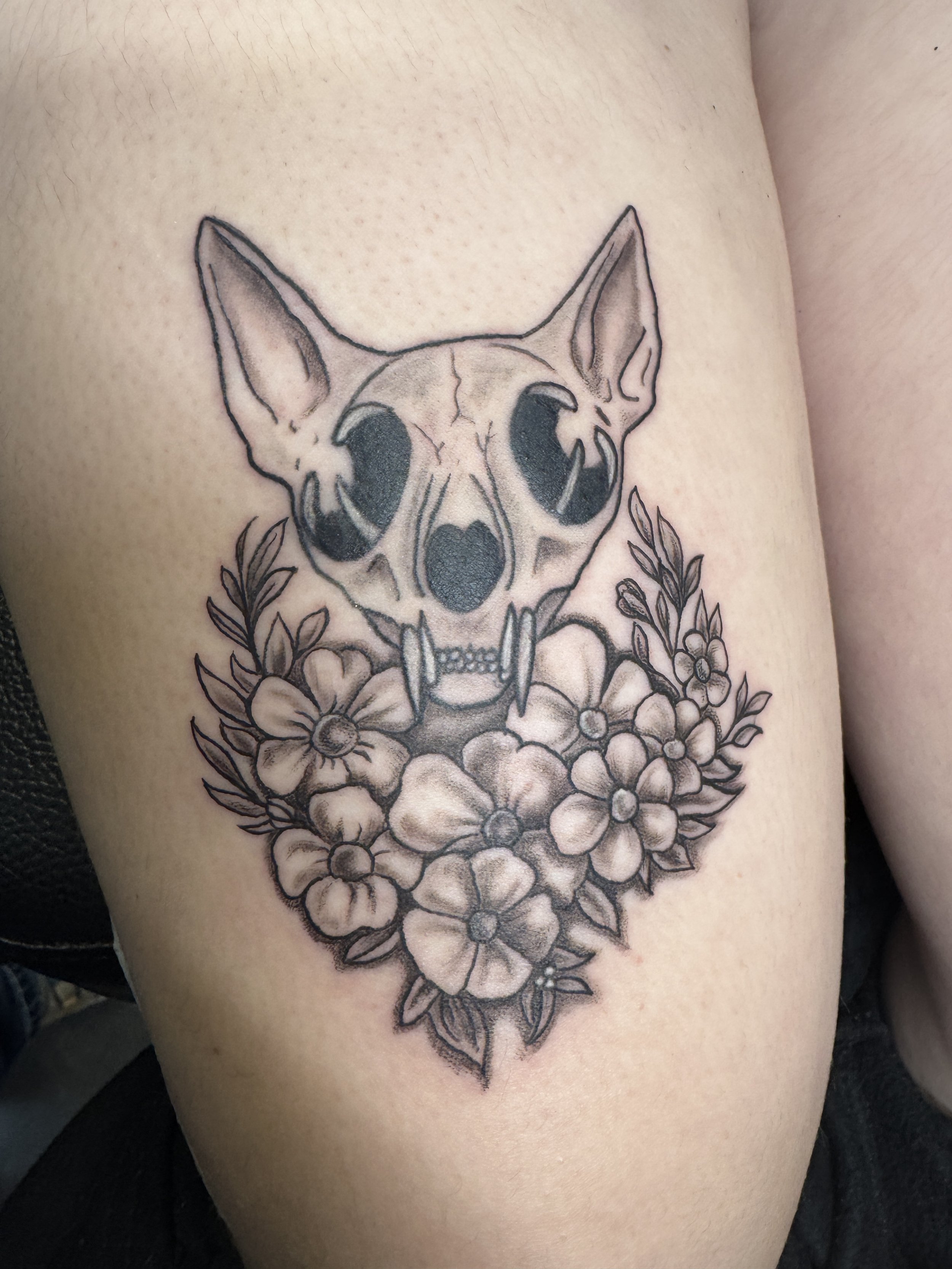 Tattoo of a dog's skull with flowers and leaves underneath.