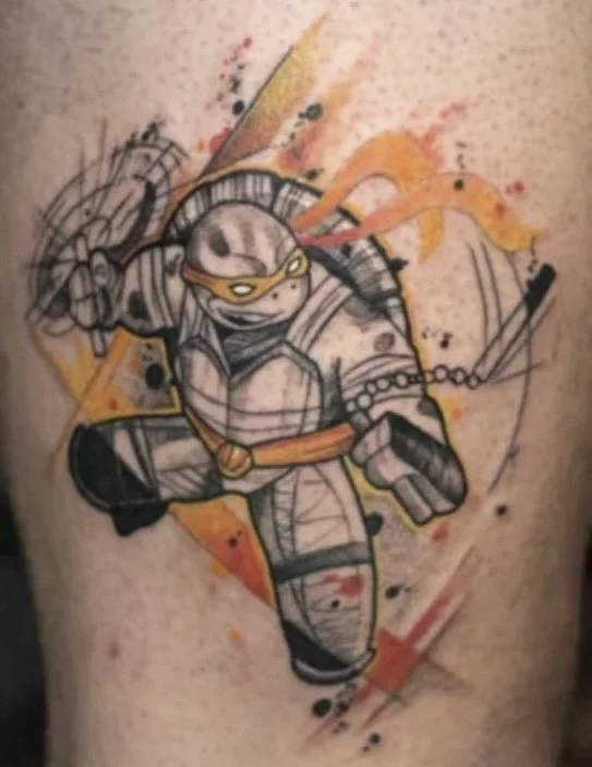 Tattoo of a Teenage Mutant Ninja Turtle, specifically Raphael, in black and gray ink with splashes of orange and yellow watercolor effects.