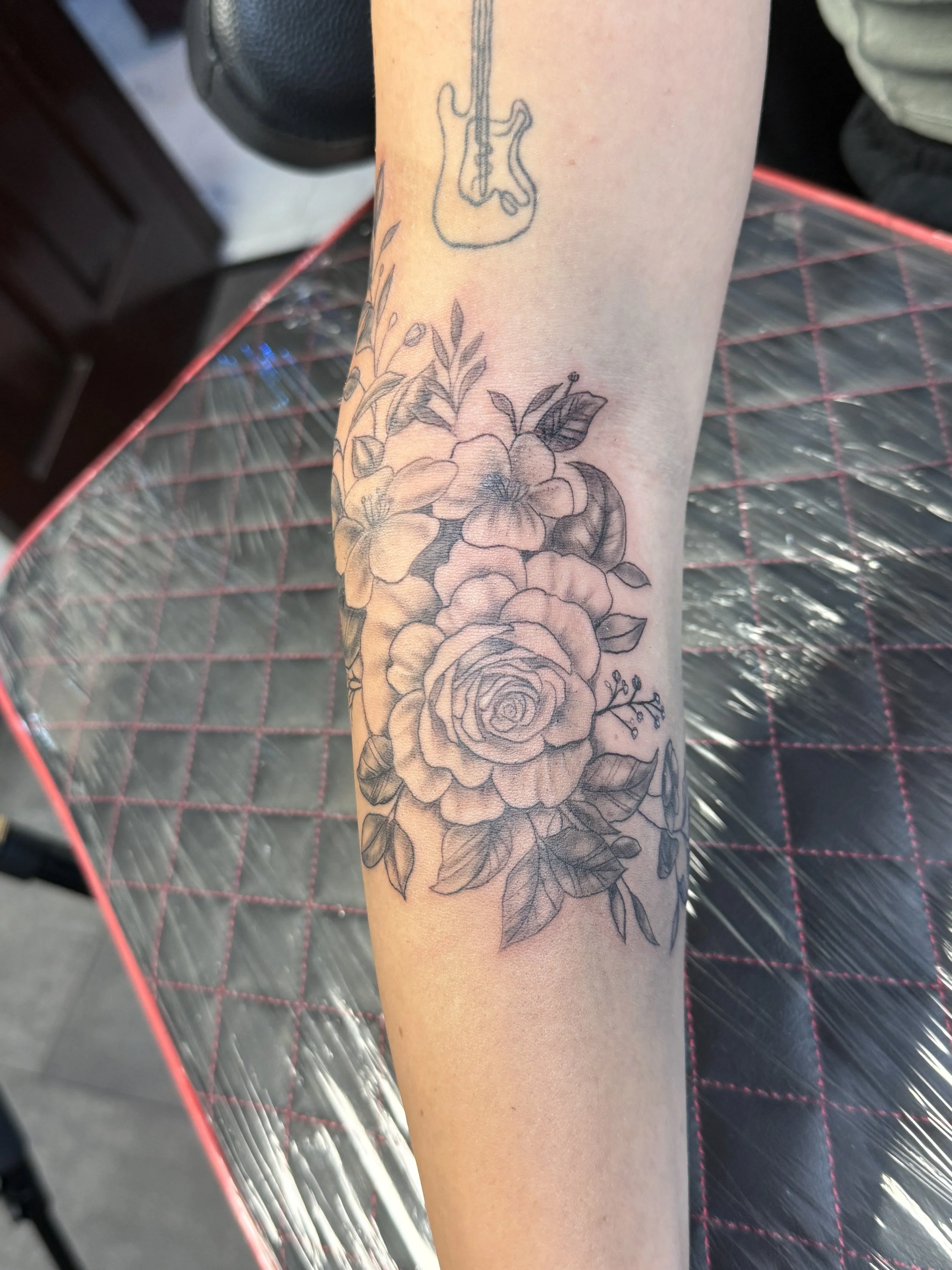 Black and gray floral tattoo on forearm featuring roses and leaves.