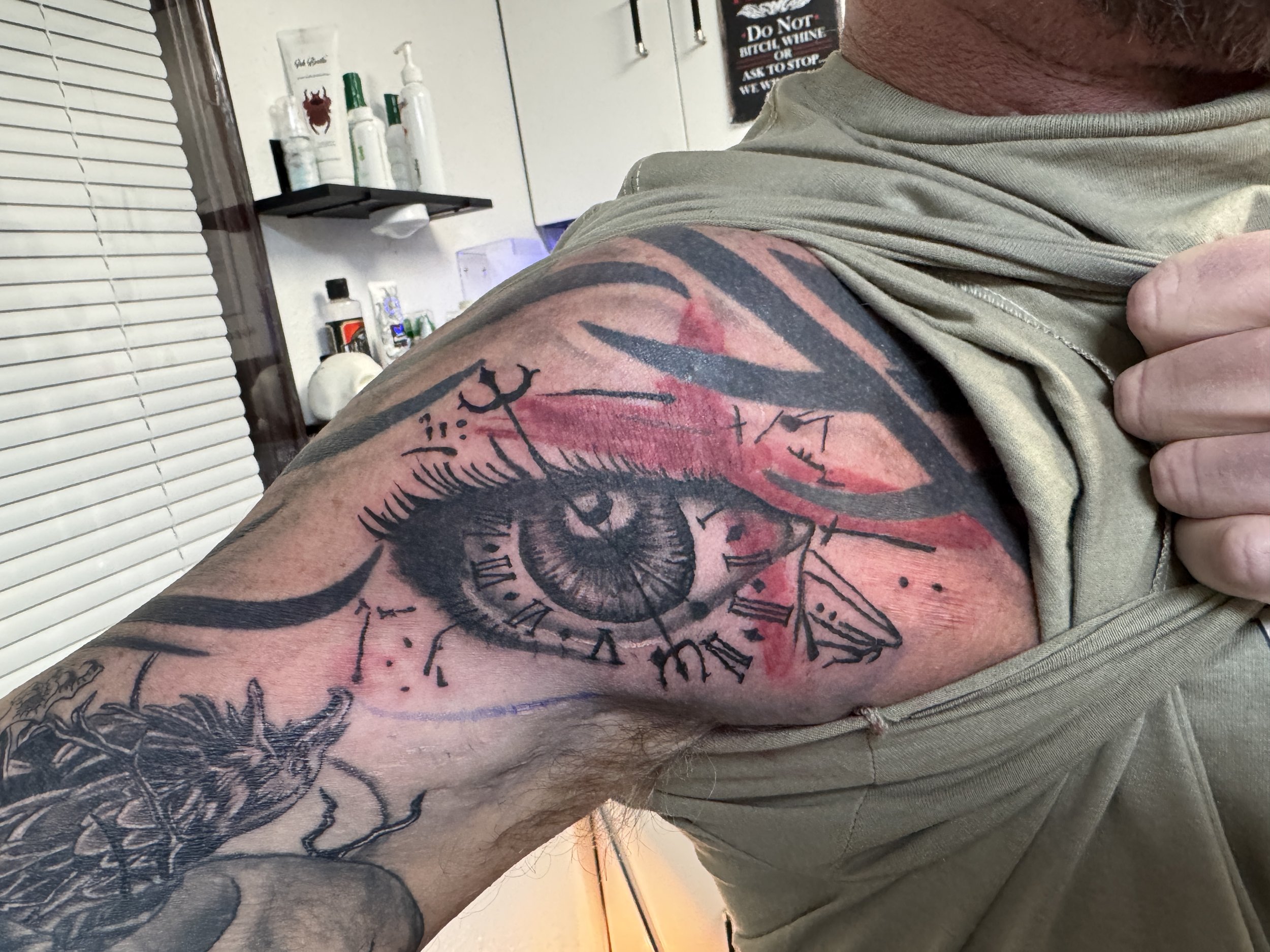 Tattoo of an eye with clockwork elements on a person's upper arm and shoulder.