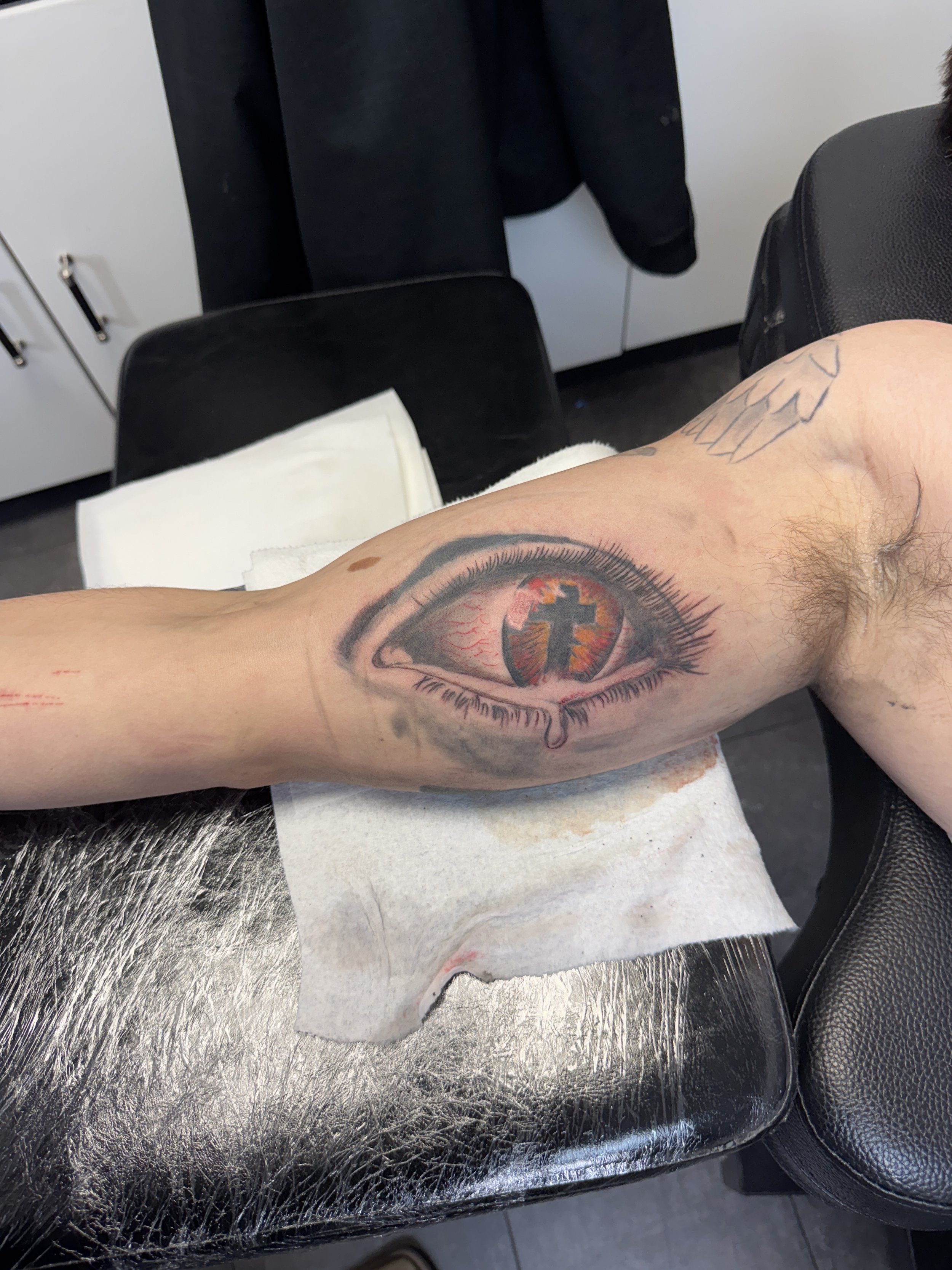 Freshly tattooed eye with a church and red flames in the iris, on a person's forearm.