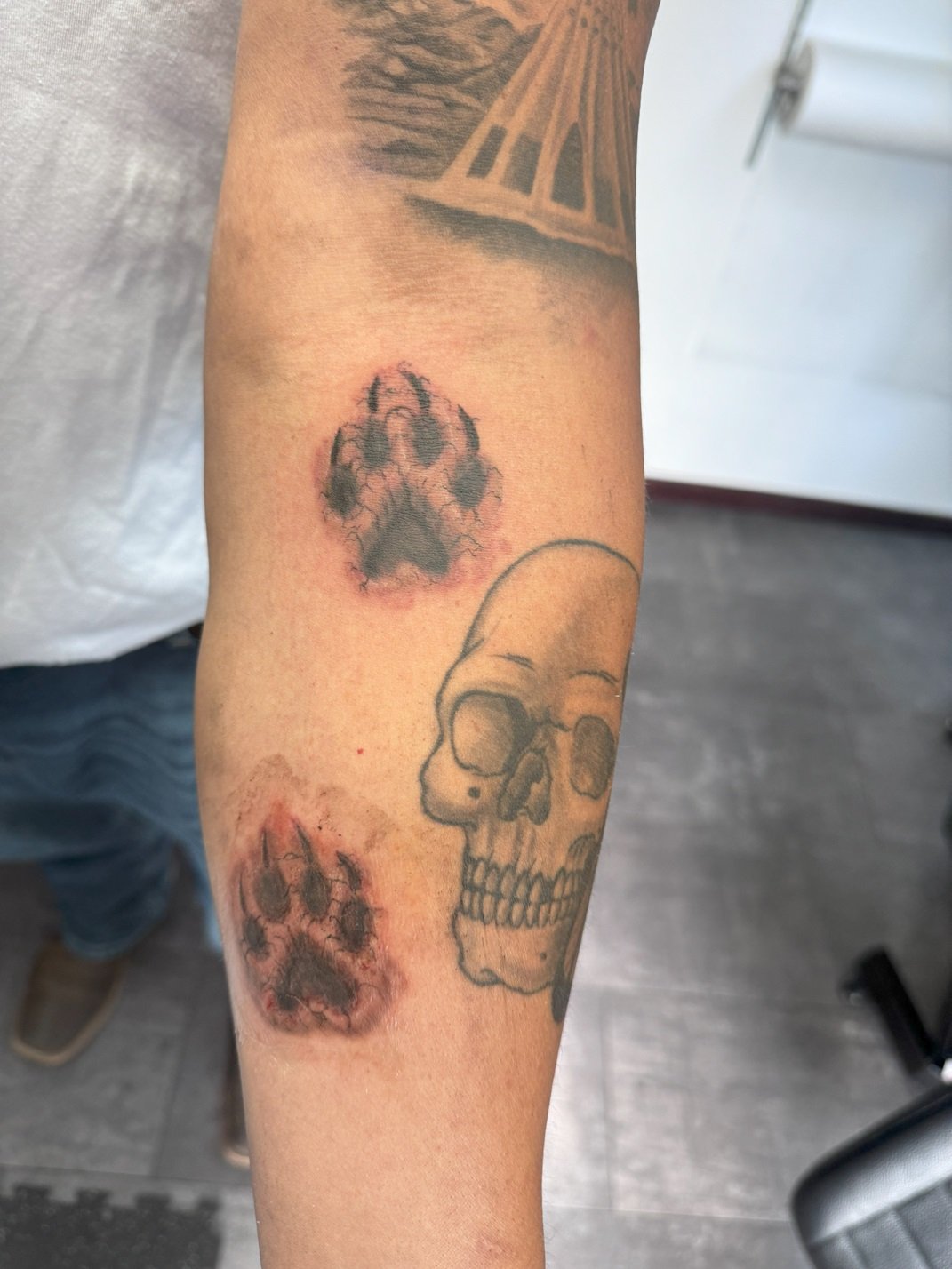 Tattoo of a skull and two paw prints on a person's forearm.