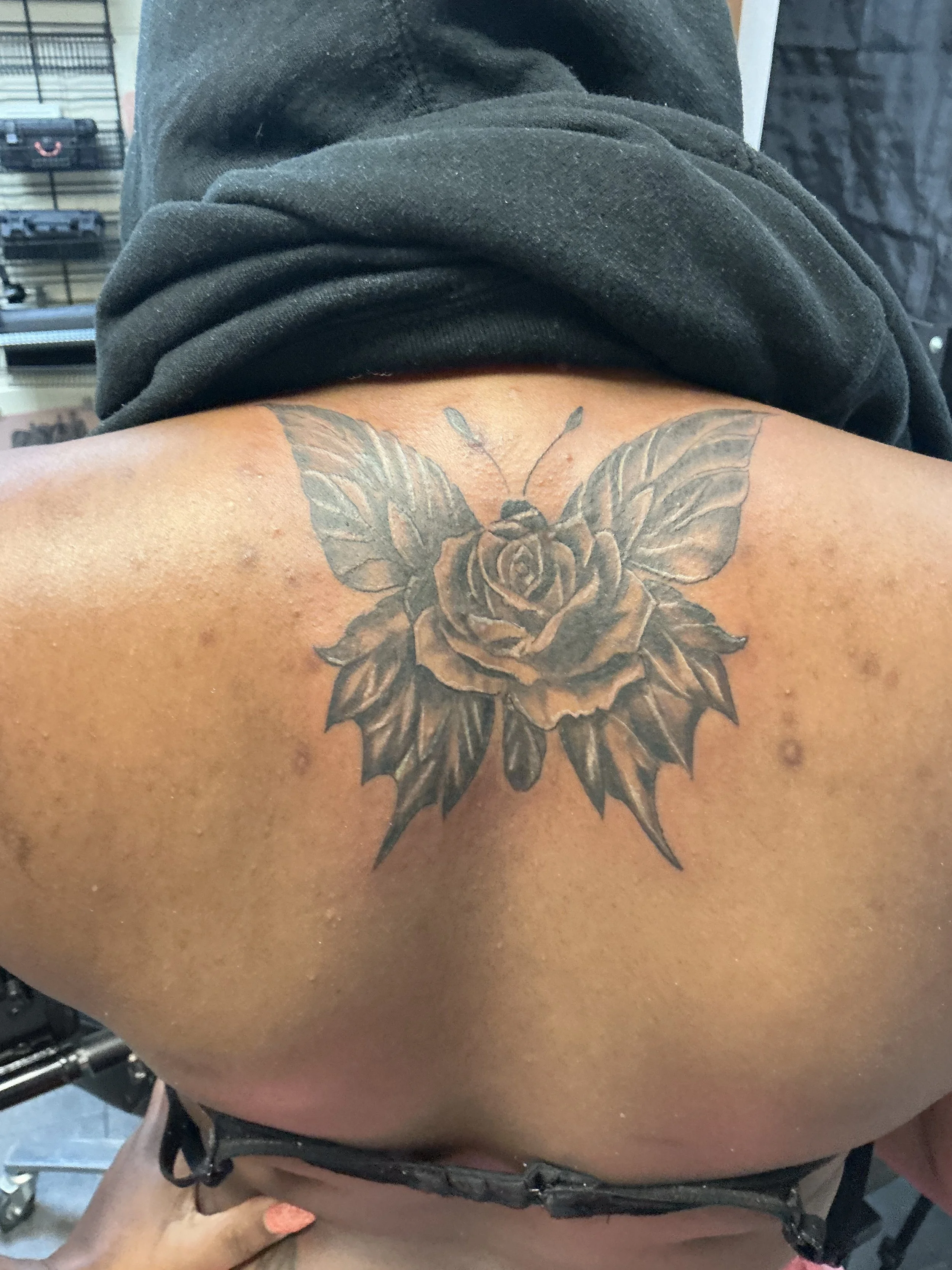 Back tattoo of a detailed black and gray rose with butterfly wings and antennae.