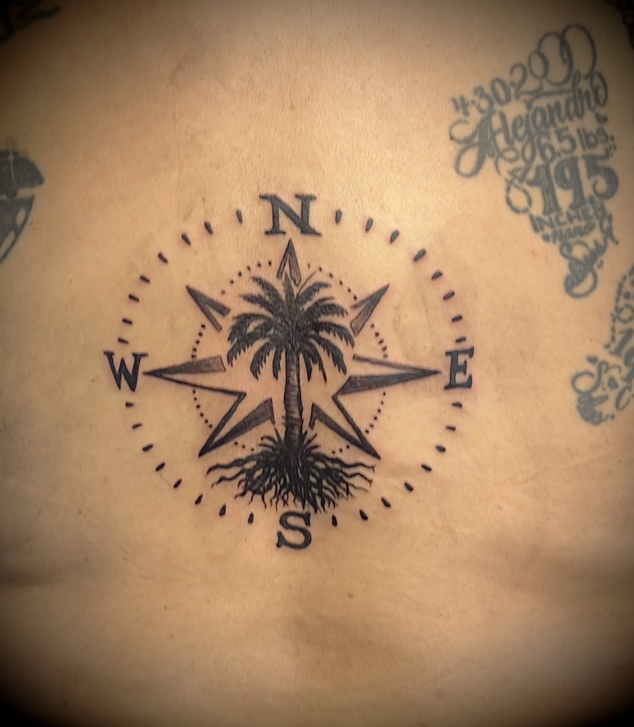 Tattoo of a compass with a palm tree in the center, on a person's skin.