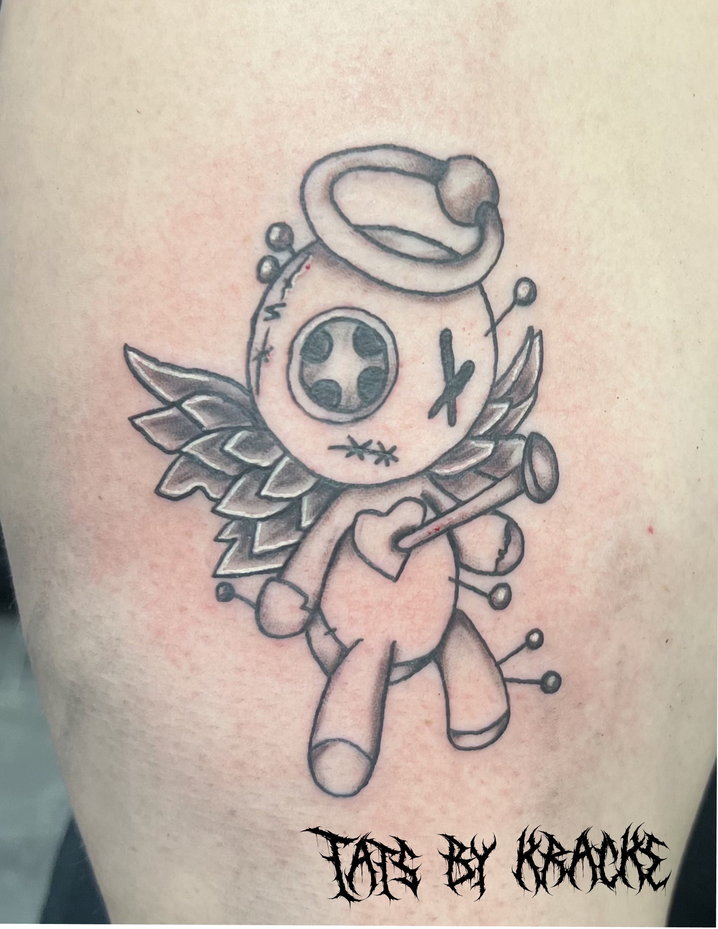 Tattoo of a cute, cartoonish creature with a stitched-up face, winged body, and a stethoscope, holding a heart and a cane, with the text 'TATTOO BY KRACKLE' underneath.
