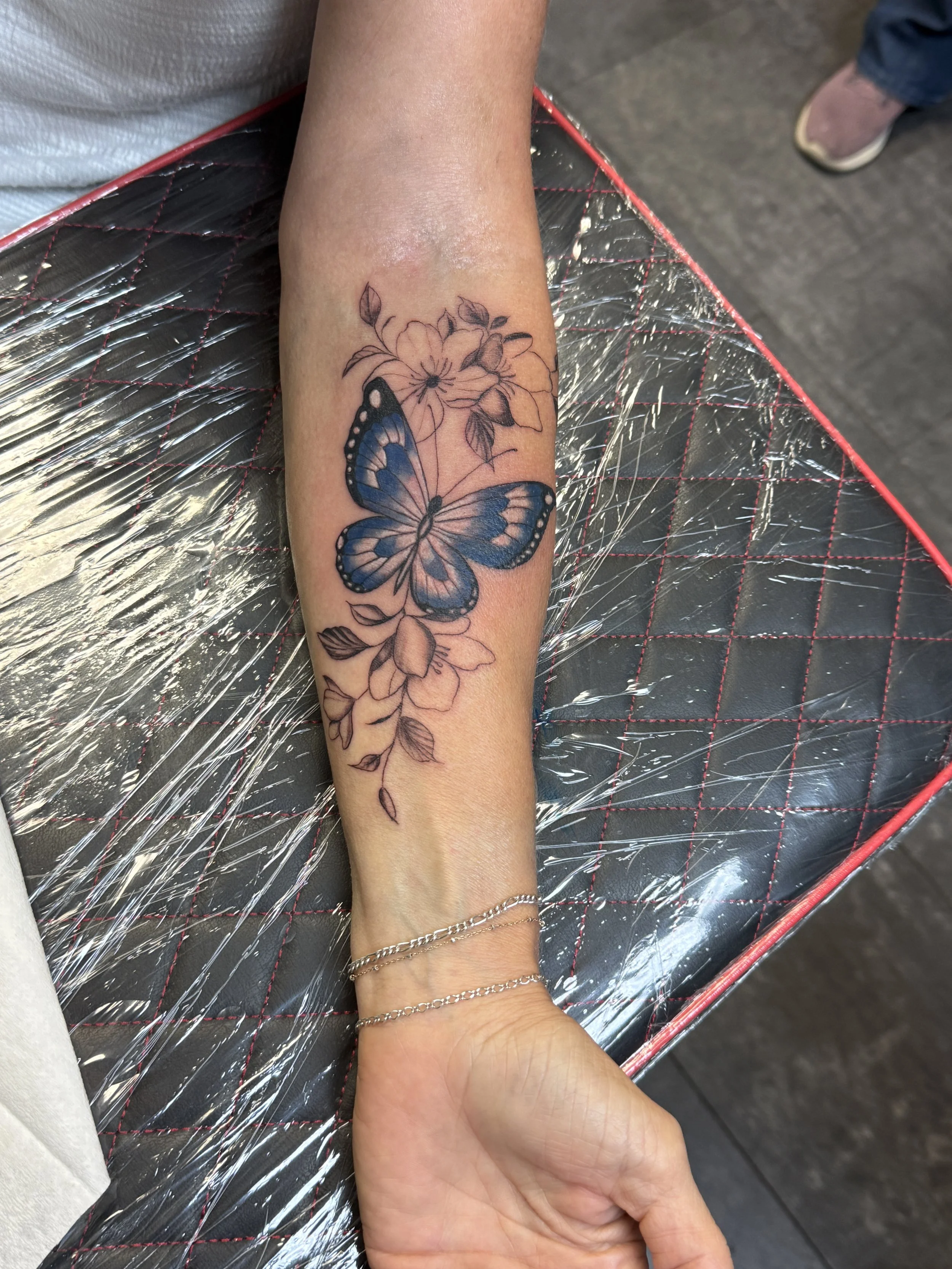Tattoo of a blue butterfly on a person's forearm with floral designs.