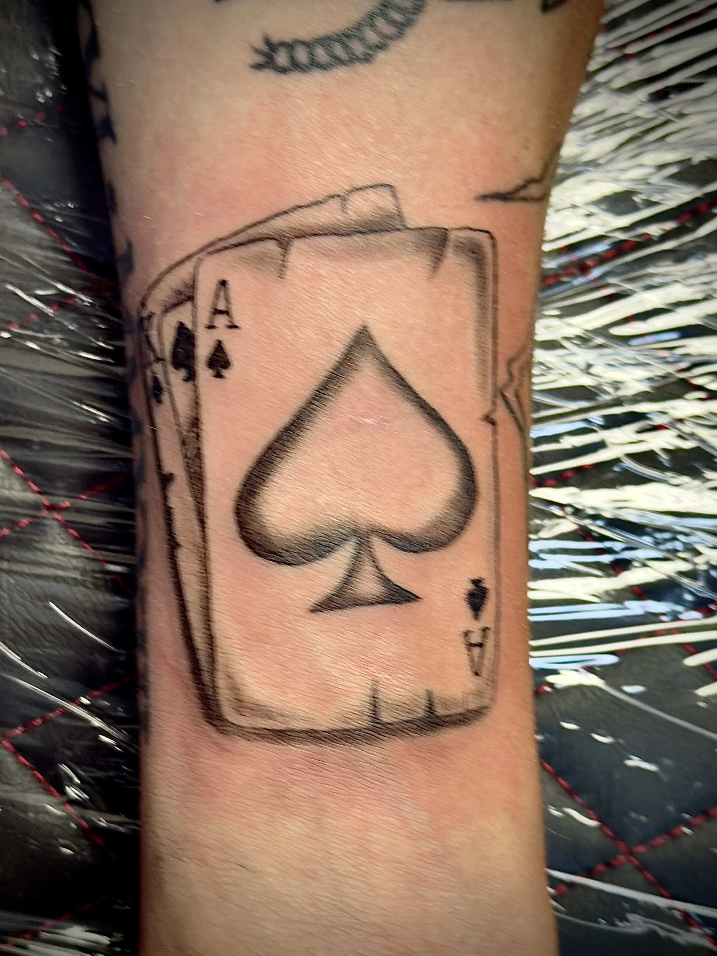 Tattoo of a playing card, the ace of spades, on a person's forearm.