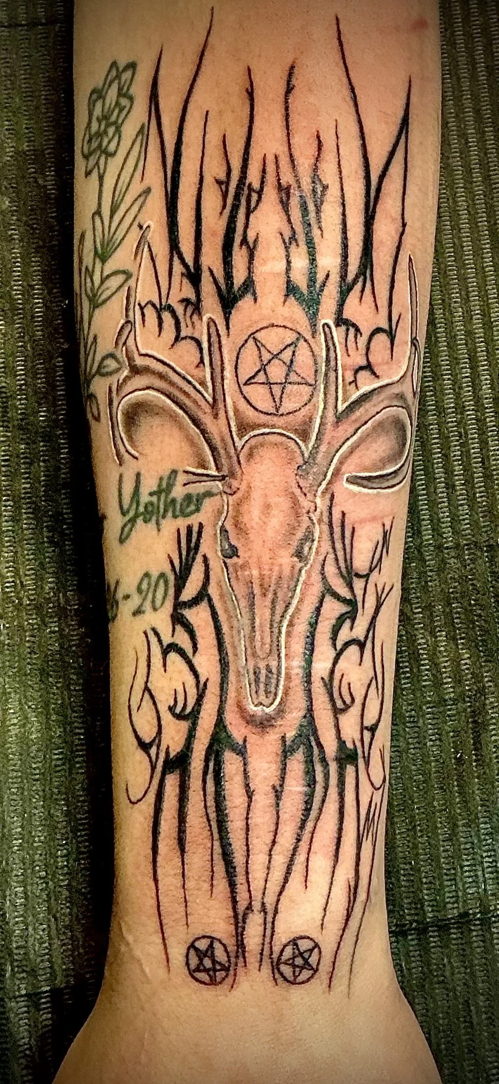 Tattoo of a deer skull with antlers, decorated with pentagrams, surrounded by abstract lines and a leaf.