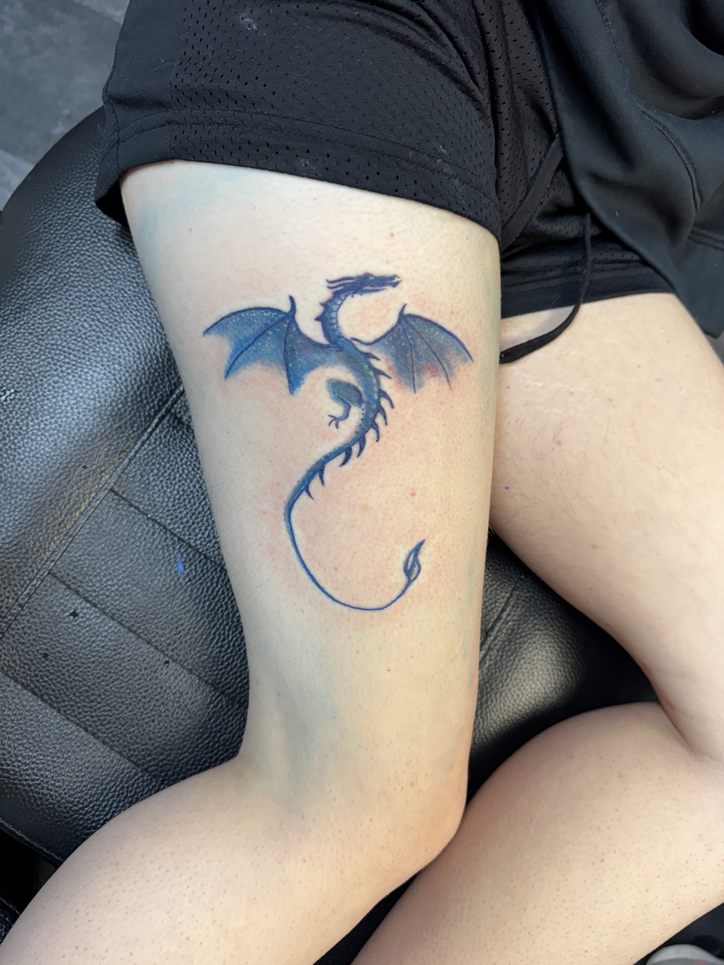 Tattoo of a blue and black dragon on a person's thigh.