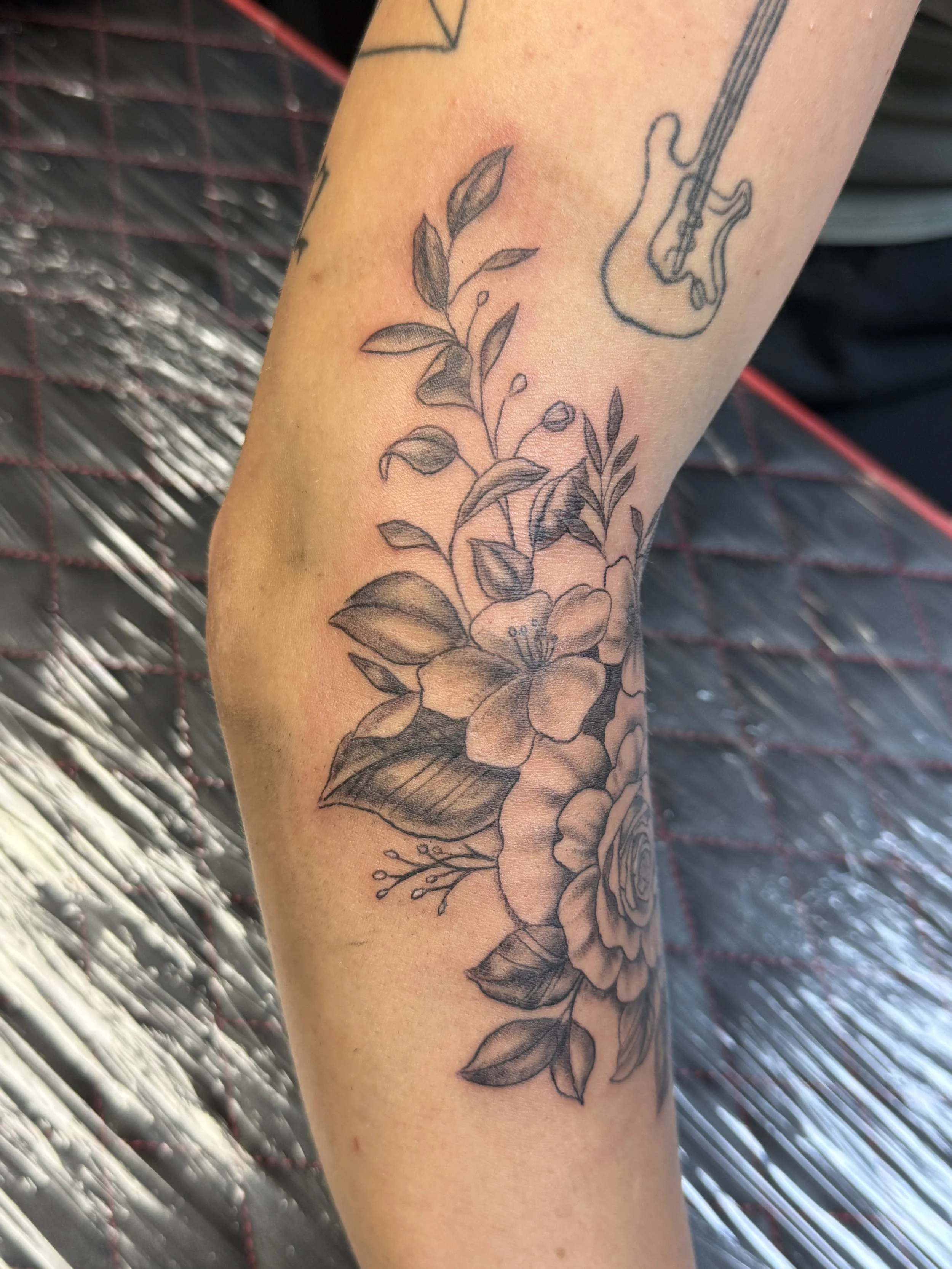 Black and gray floral tattoo featuring a large flower with multiple leaves on the forearm.