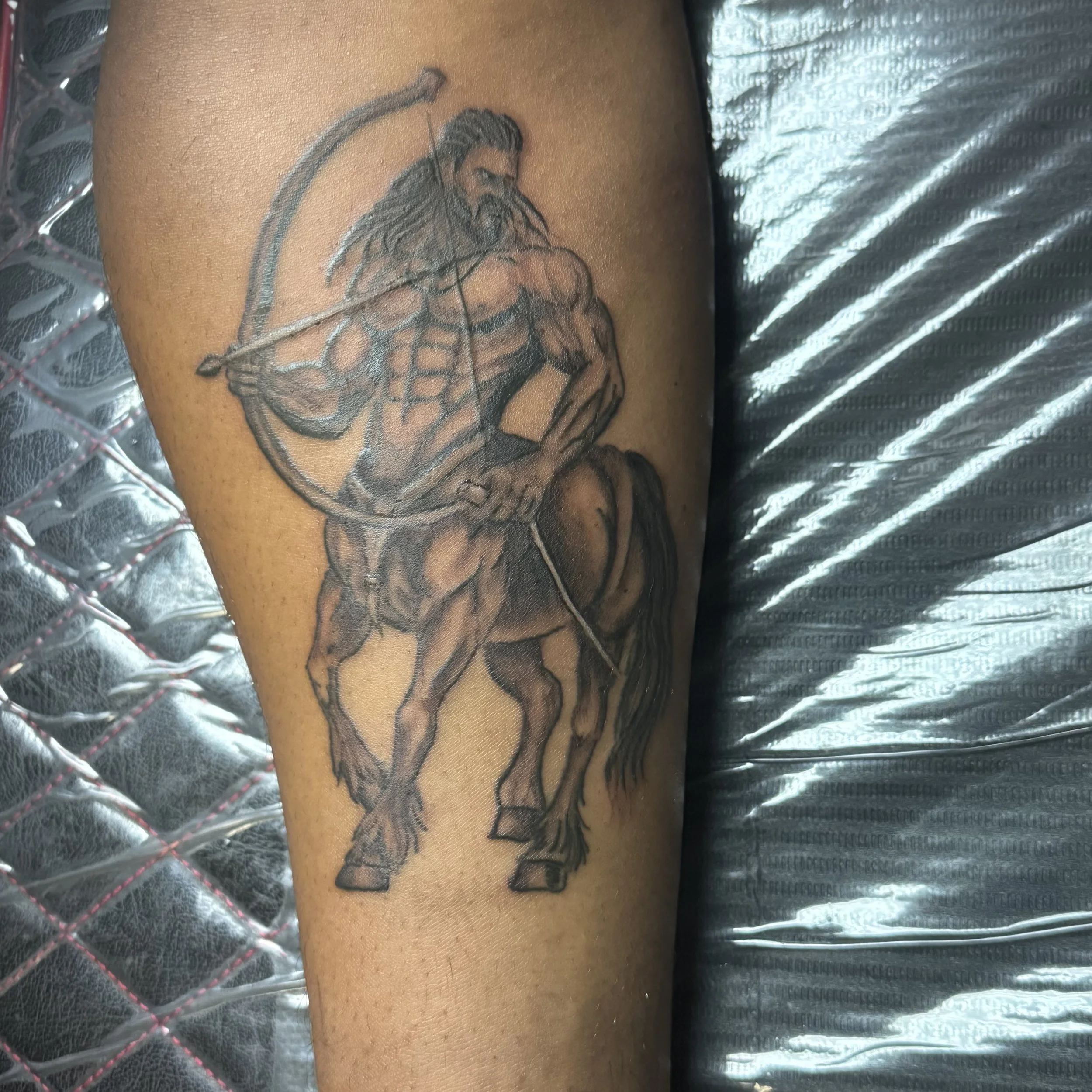 Tattoo of a muscular man riding a horse, holding a bow and arrow, on upper arm.