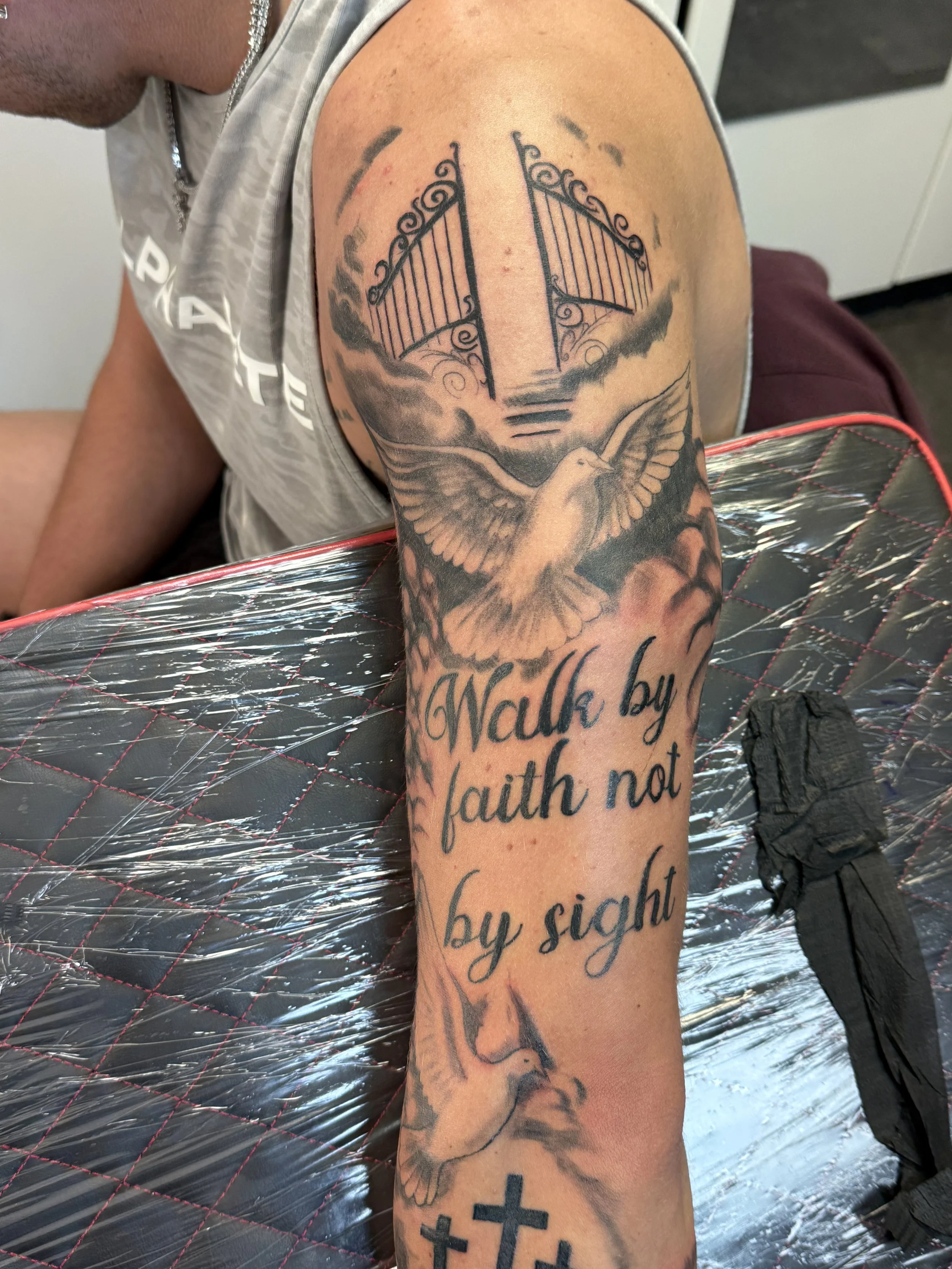 Tattoo of a bird and a boat gate above a quote that reads 'Walk by faith not by sight' on a person's arm.