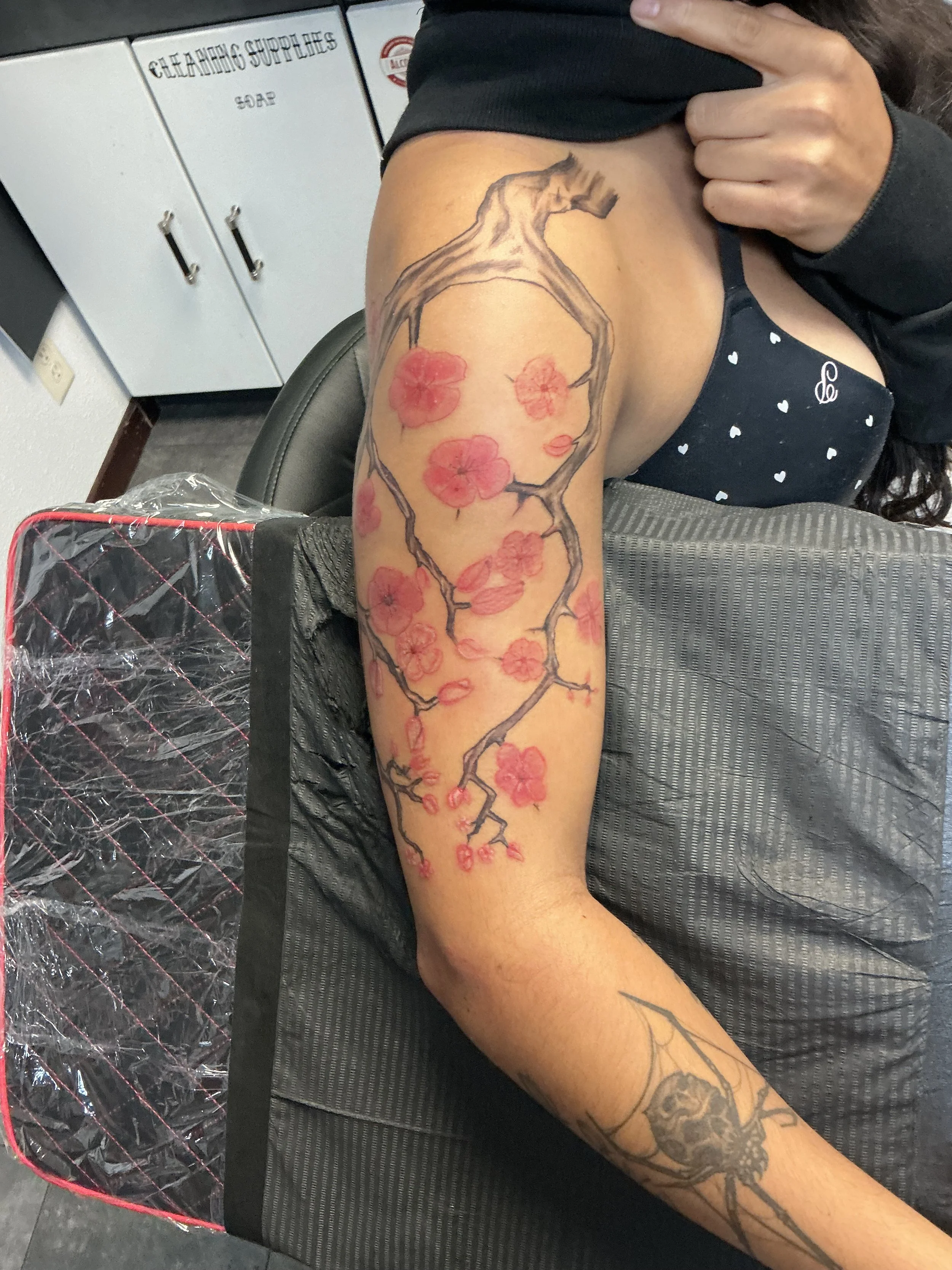 Tattoo of a cherry blossom branch with pink flowers on a person's upper arm and shoulder.