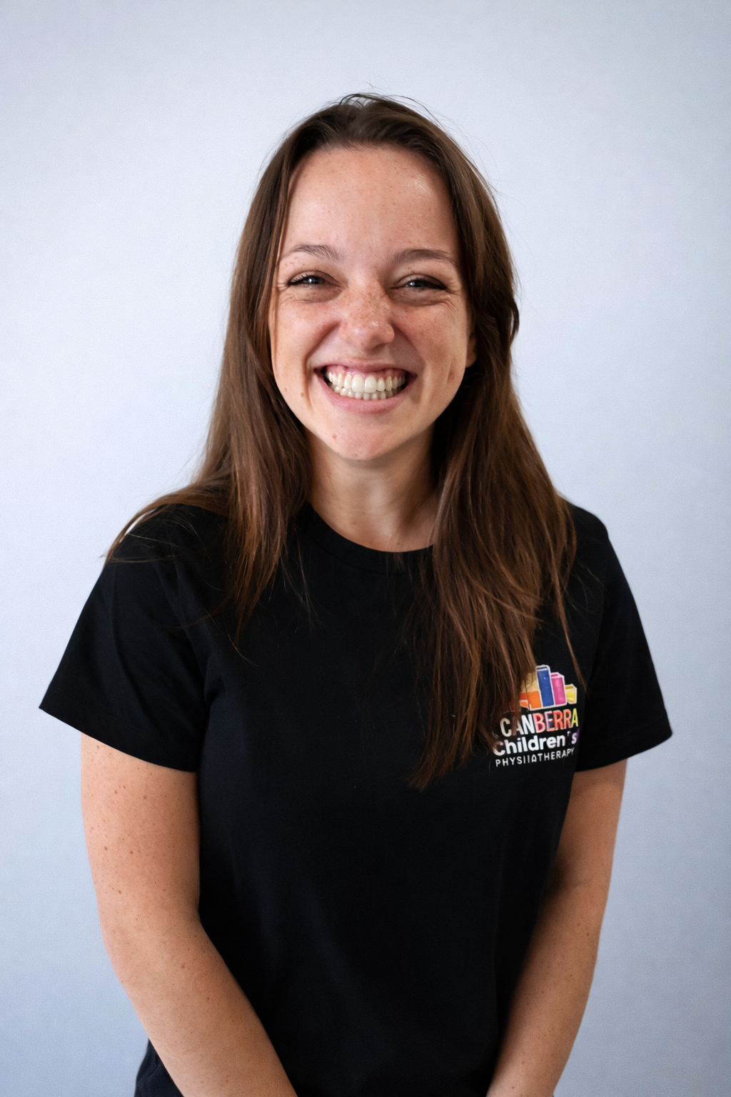 Woman with light brown hair, smiling, wearing black t shirt against white background.