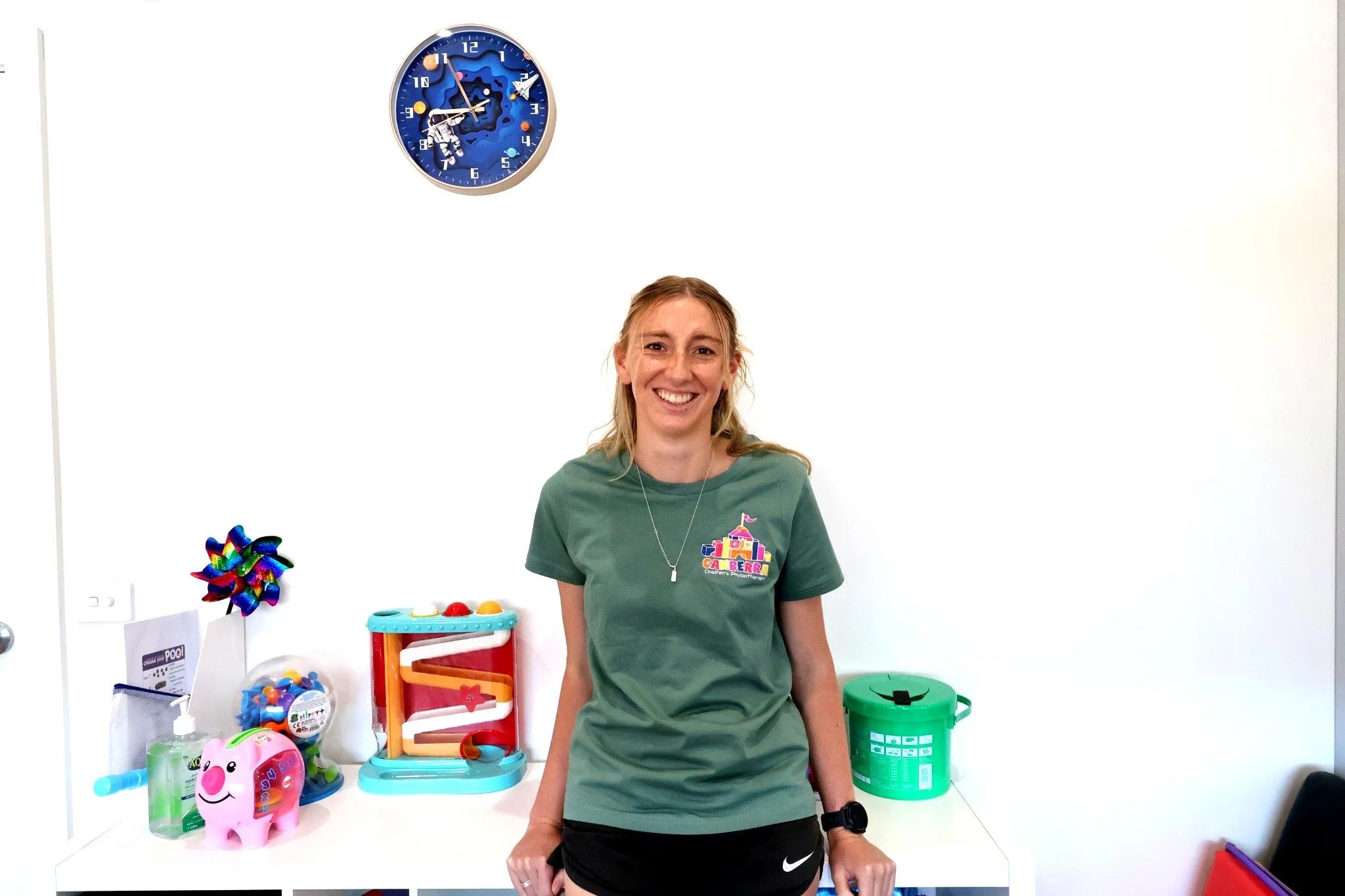 Smiling Woman, Green Shirt, on white background with blue clock in upper left corner