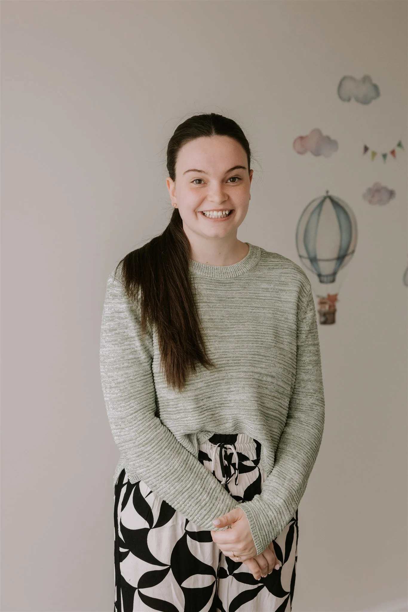Kate Princehorn - PT - Young Woman with brown hair in a pony tail to the side, gray sweater, smiling.