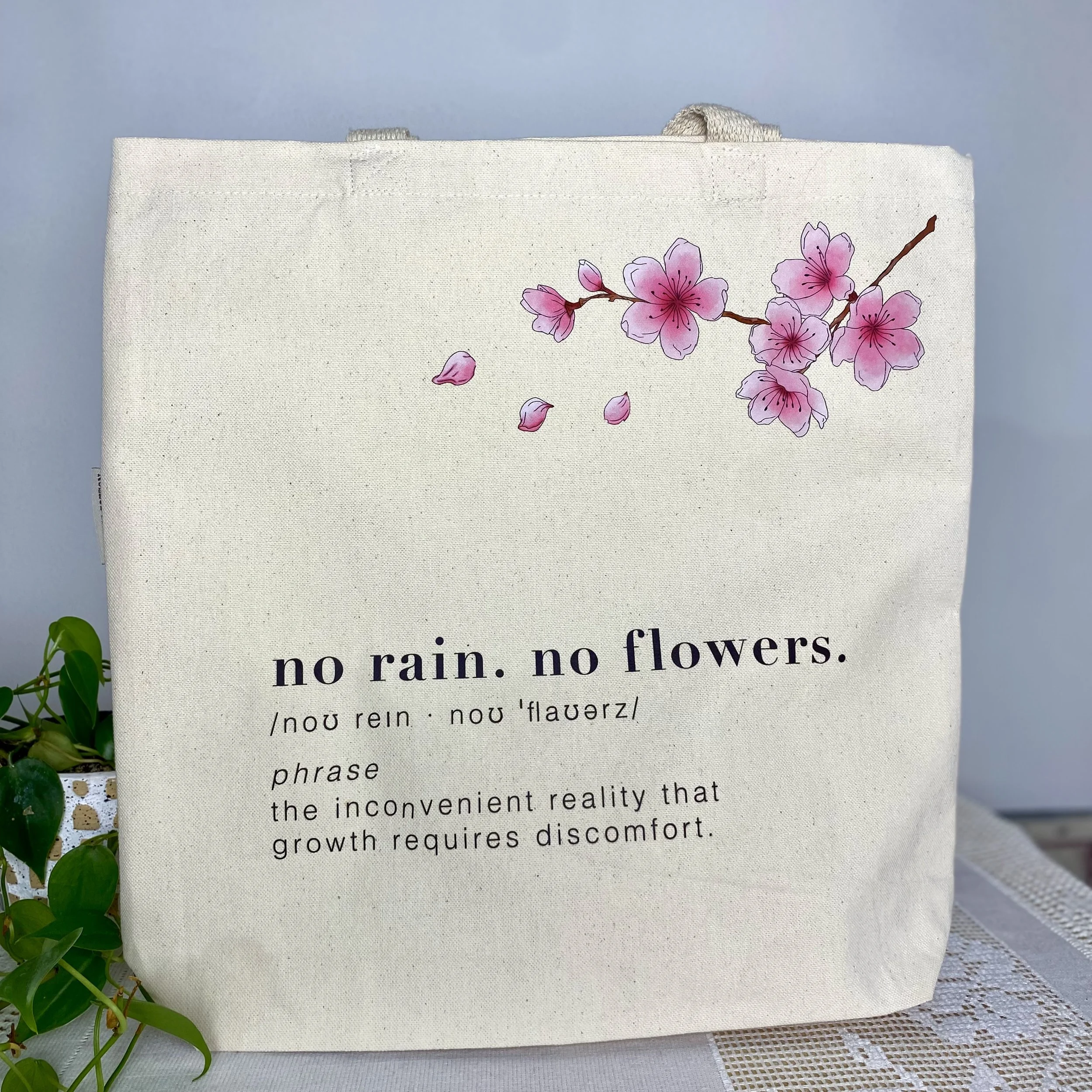 100% Organic Cotton canvas bag with cherry blossom graphic and the phrase no rain no flowers. 
