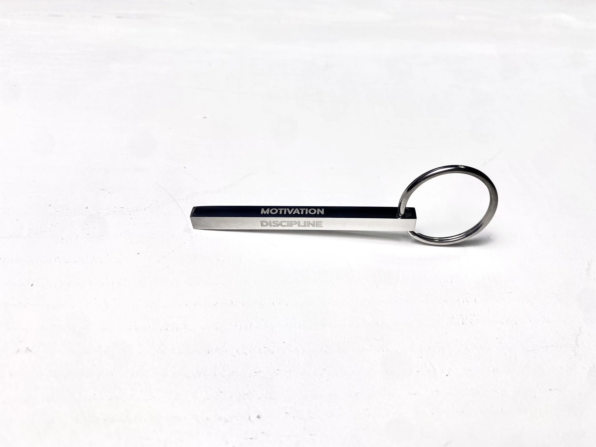 Sleek minimalist silver metal bar keychain with words "DISCIPLINE CONSISTENCY MOTIVATION DETERMINATION" on it.
