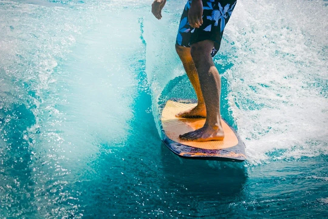 Close-up of a person surfing on a wave, wearing blue swim shorts, with their foot positioned on the surfboard.