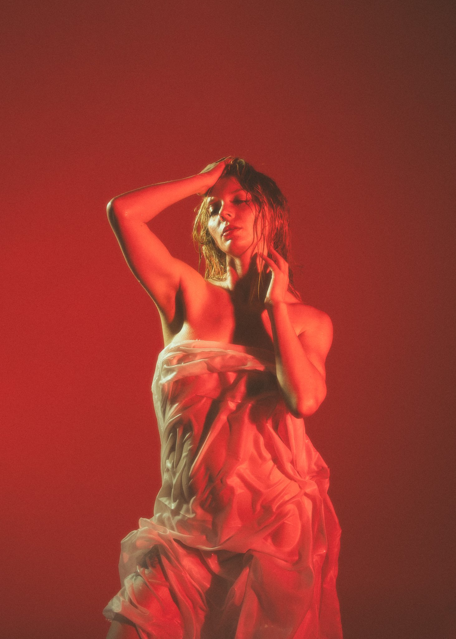 Woman wrapped in white fabric with red lighting, artistic pose.