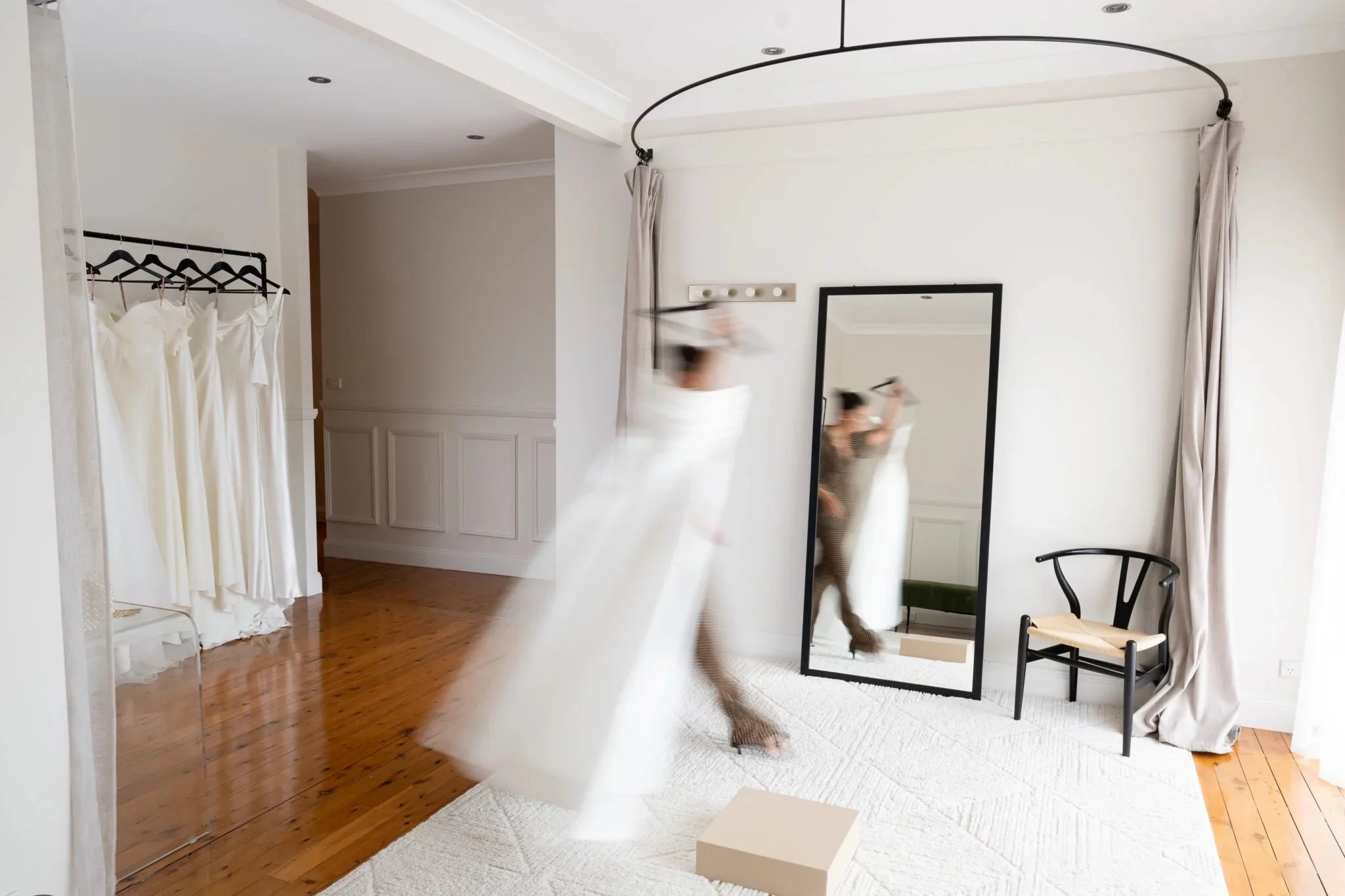 Bright bridal boutique with wedding gowns on display and a blurred figure carrying a dress