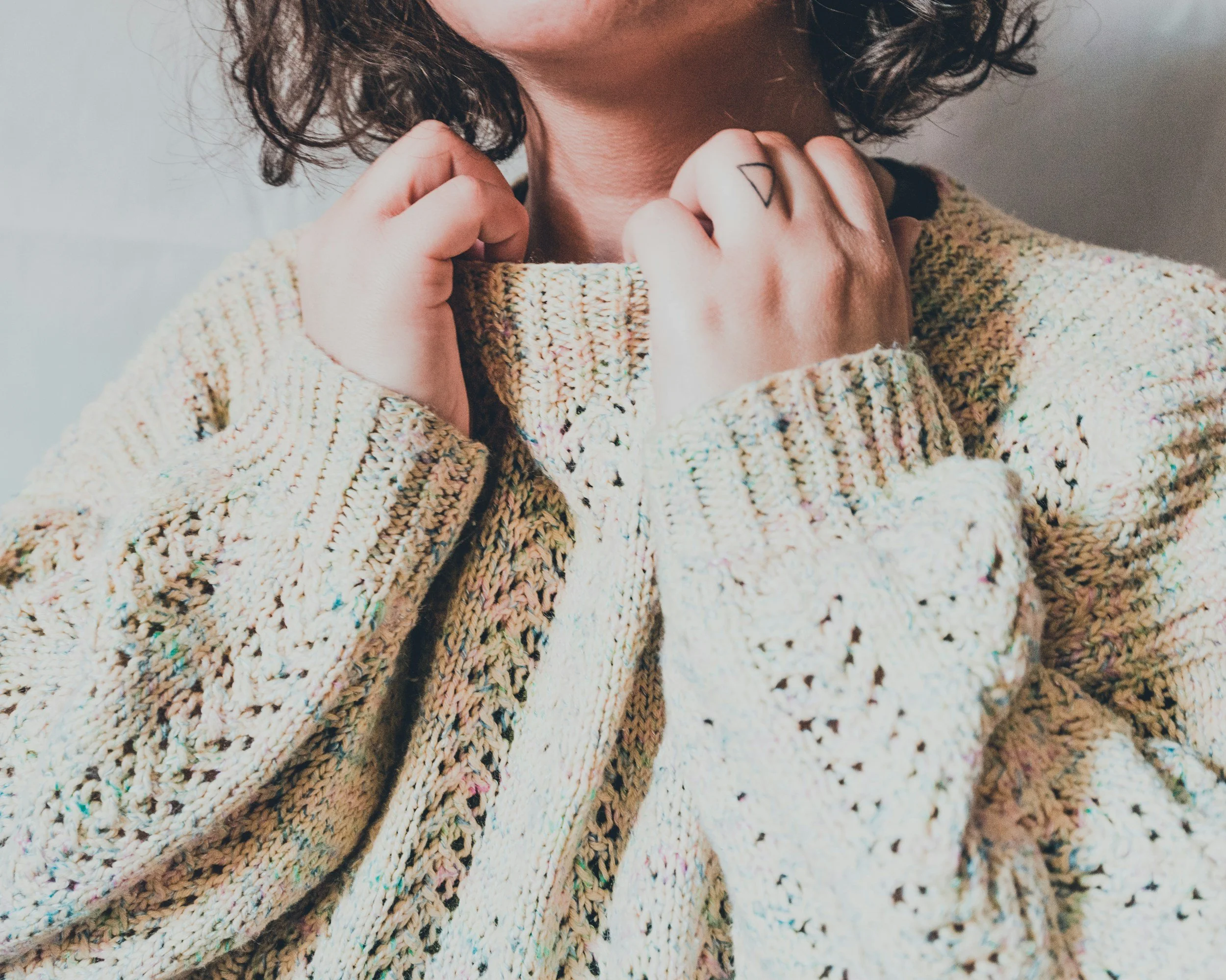 Close-up of a person's hands clasped at the collar of a knitted jumper.