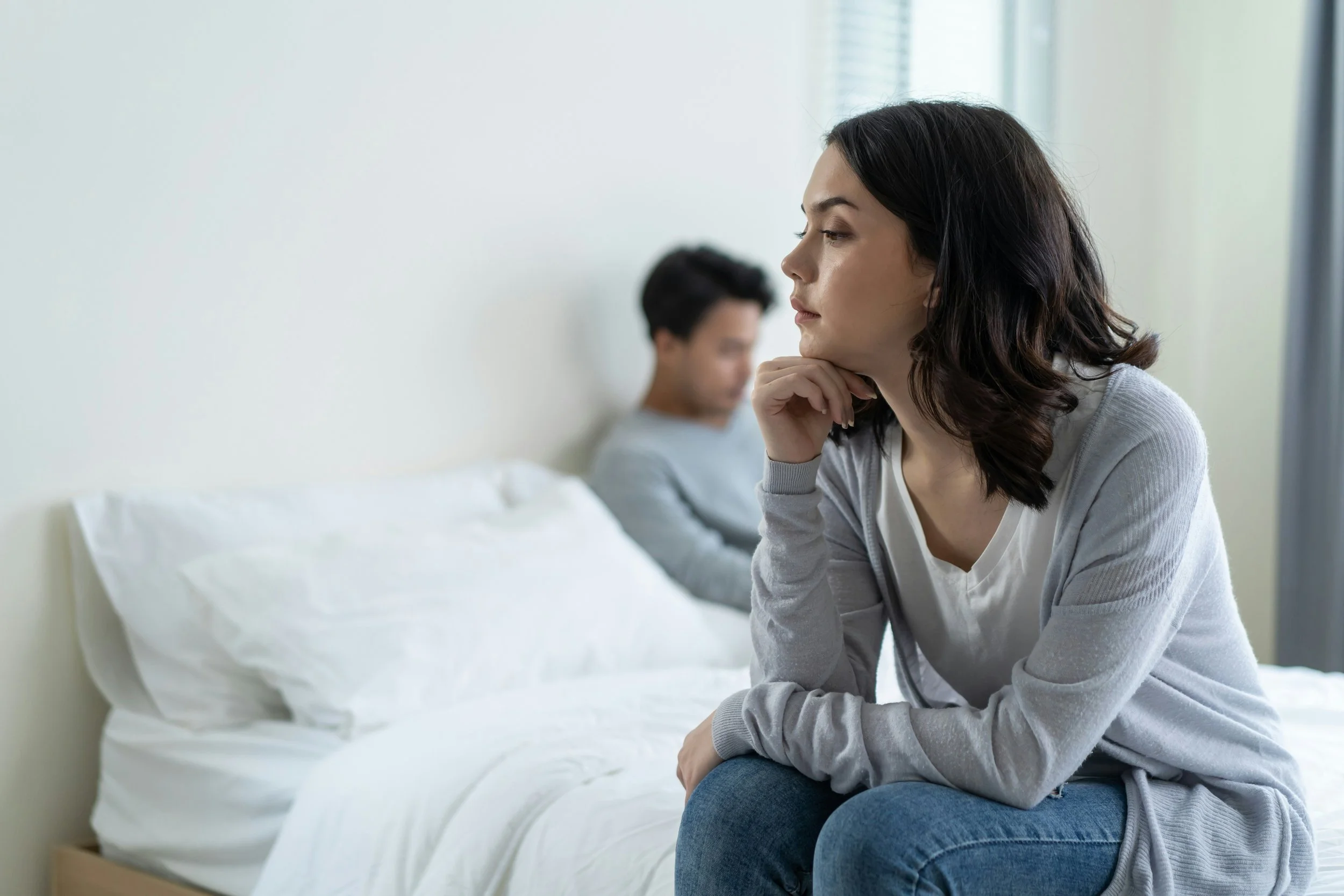 Two people sitting apart on a bed, both looking away.