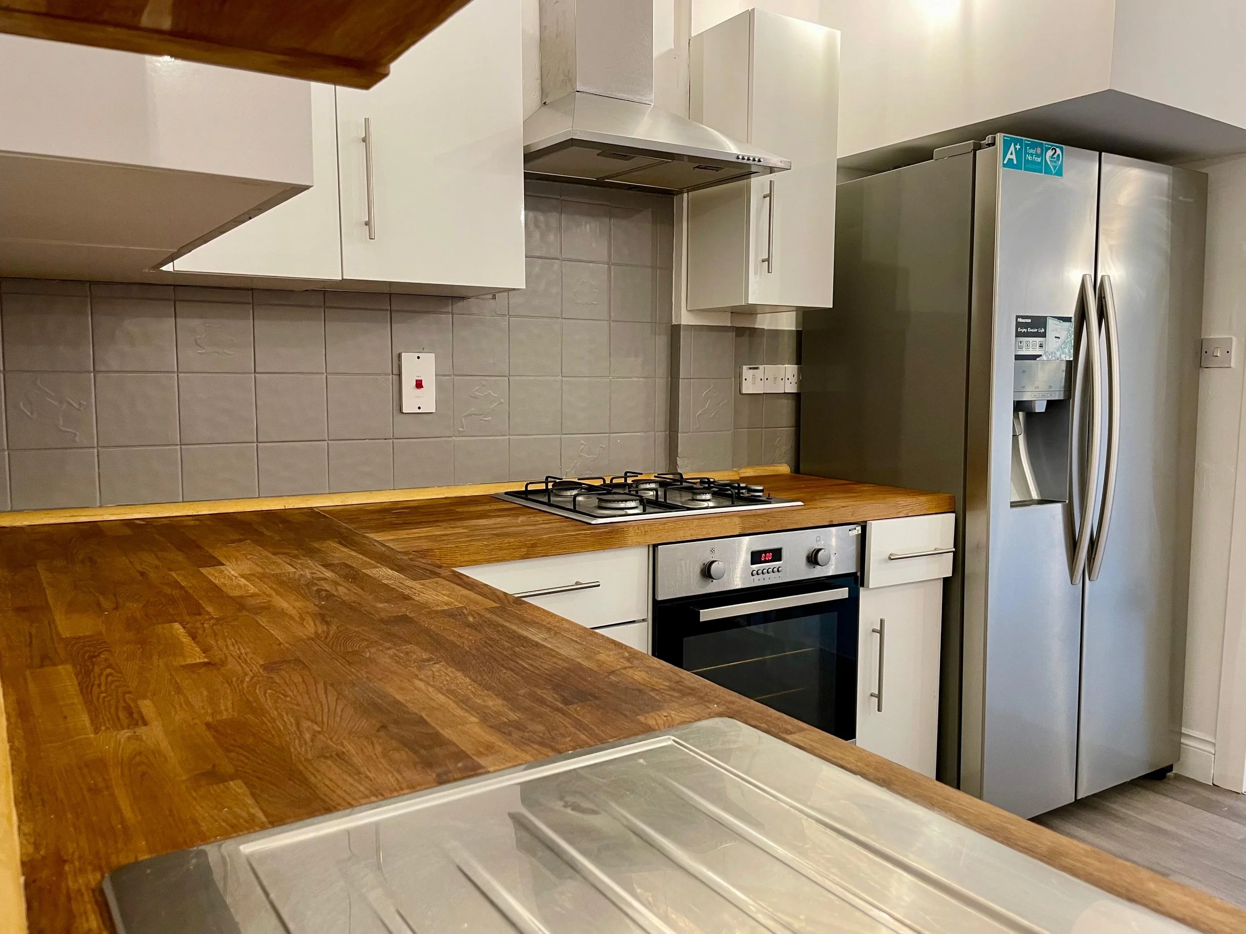 Modern kitchen with wooden countertop, gray tiled backsplash, white cabinets, stainless steel refrigerator, oven, and stove with four burners.